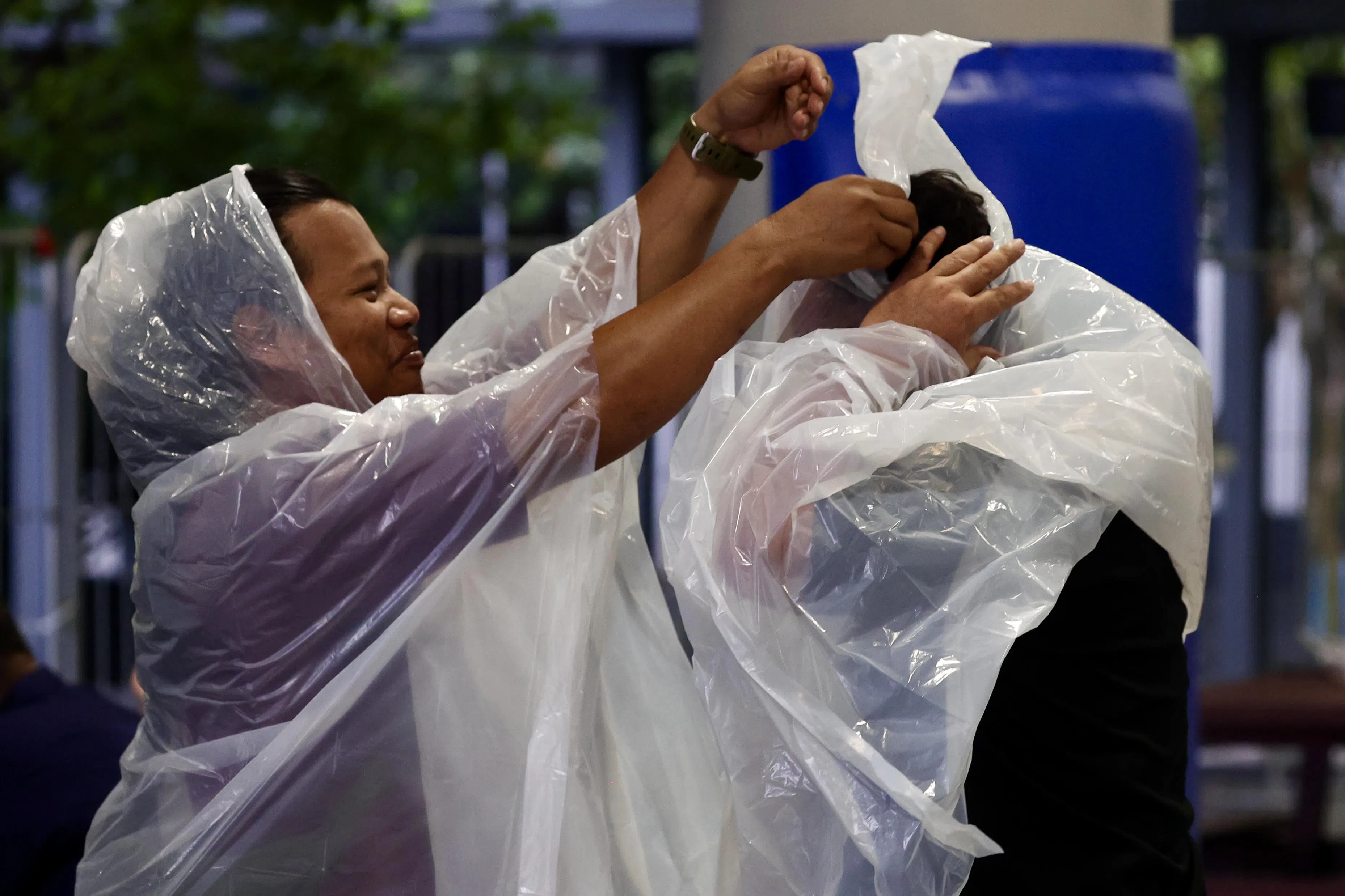 红点同心党4月29日在新加坡科技中学举行群众大会。虽然现场天不作美，但出席者互相帮忙，为彼此套上雨衣。（陈斌勤摄）