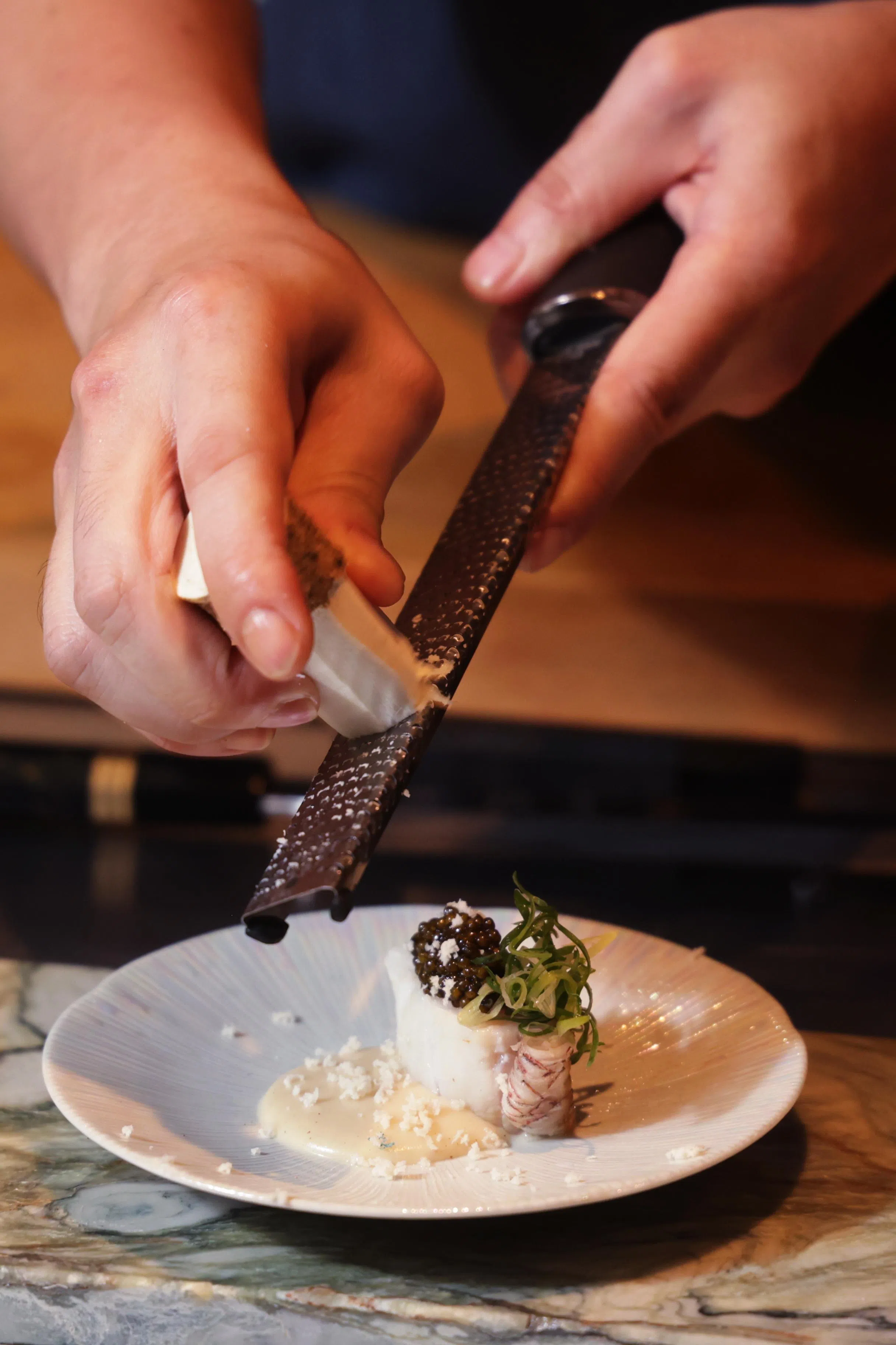 黎司诺在烹煮炭火烧长崎赤鲑鱼佐白蘑菇奶油酱与卡露伽鱼子酱，其上铺上辣根刨片，为菜式增添一抹辛辣刺激感，使鱼肉的鲜美和奶油酱的浓郁达到完美平衡。（蔡家增摄）