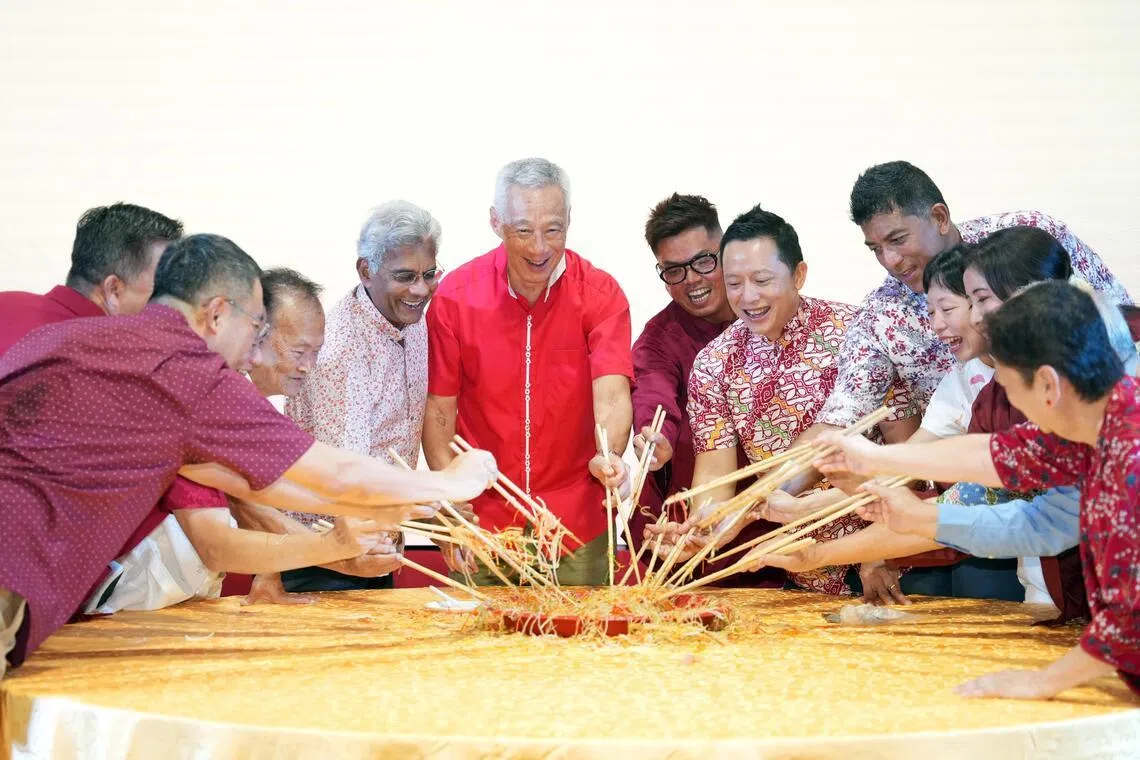 国务资政李显龙（中间）携宏茂桥集选区议员和基层领袖，在德义区新春晚宴上捞鱼生。（谢智扬摄）