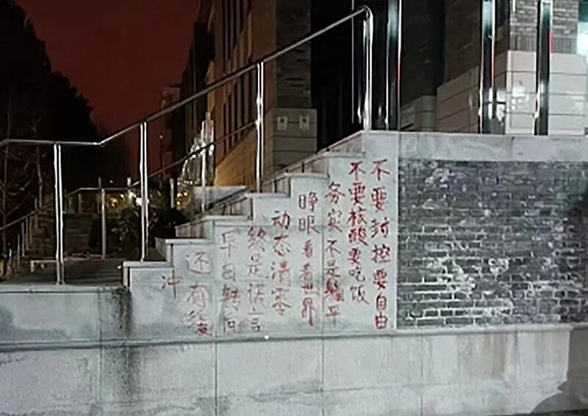 北京大学餐饮综合中心外的楼梯墙上，有红漆书写的“不要封控要自由/不要核酸要吃饭/务实不是躺平/睁眼看世界/动态清零终是谎言/早日转向还有缓冲”抗议口号。（读者提供）