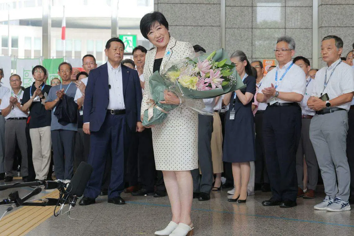 在东京都知事选举中第三次连任后，小池百合子（中）星期一（7月8日）手捧一束鲜花脸带微笑抵达东京都厅大楼。（法新社）