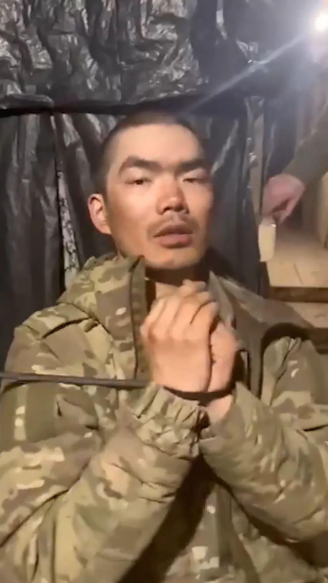 一名身穿军服的亚裔男子双手被绑，在镜头前以中英夹杂的语言比划并模仿战斗时的情况。（泽连斯基X平台截图）