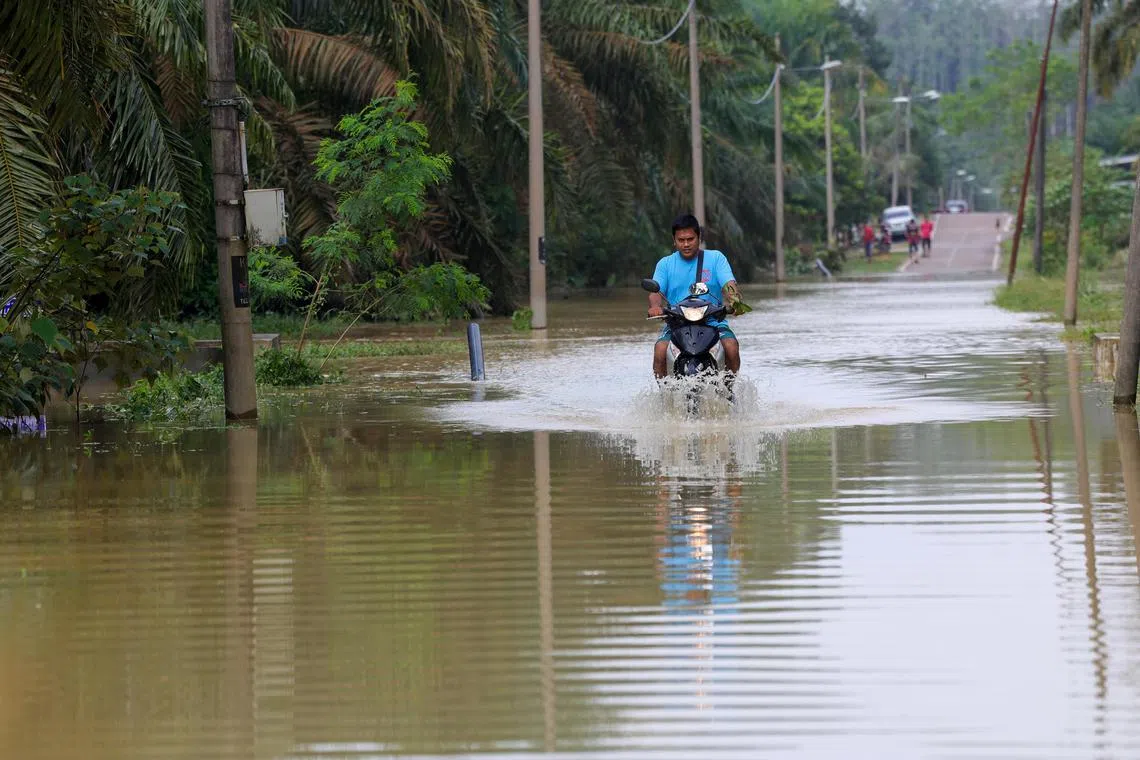 积水导致许多道路变成水路，民众骑着电单车小心翼翼涉水而过。（马新社）