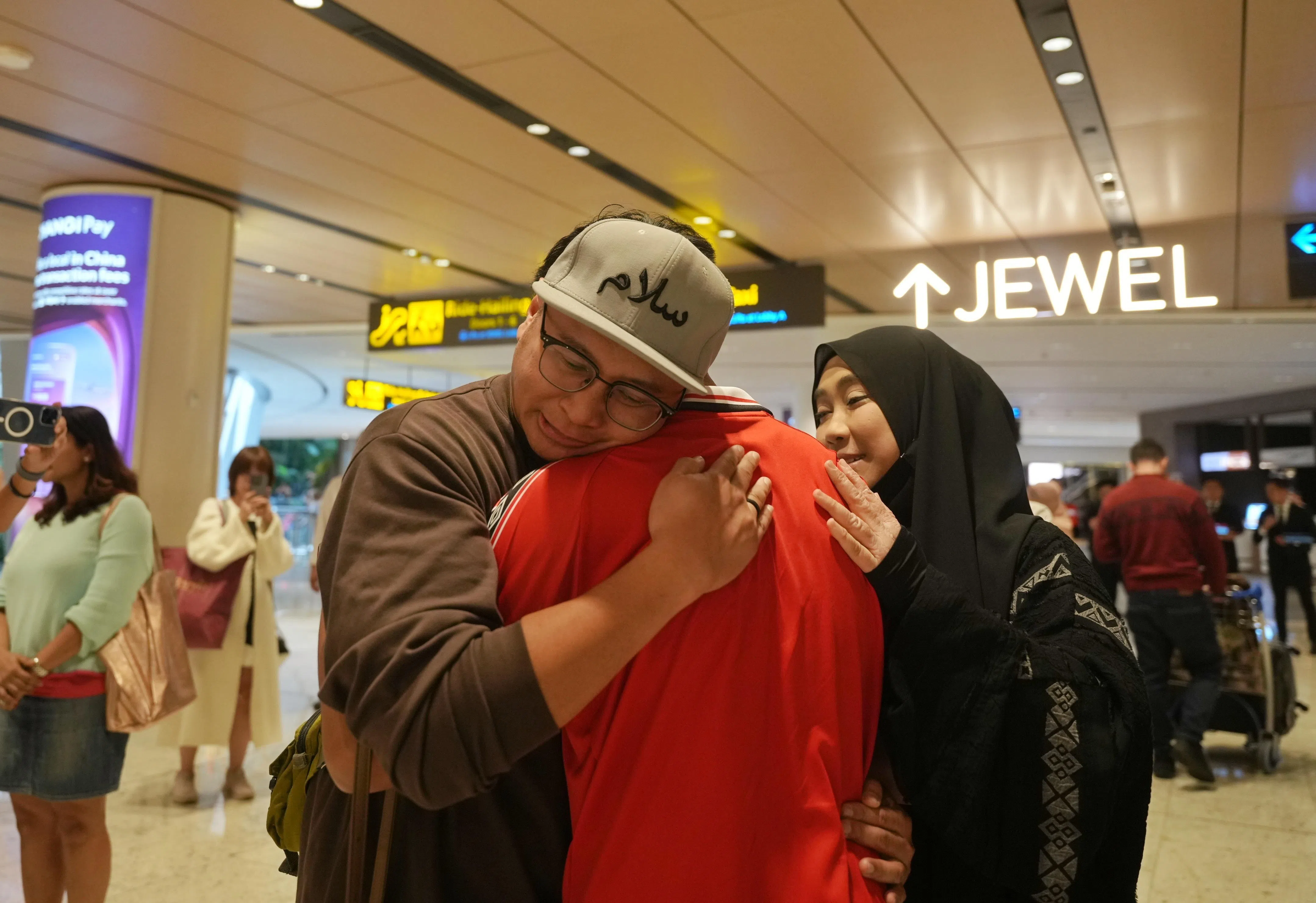 乘坐阿联酋航空客机安全返新的乘客落地后，与亲友相拥而泣。（谢智扬摄）