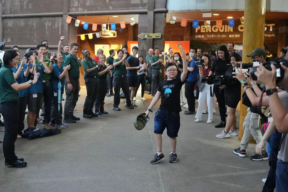 接近打烊时，裕廊飞禽公园的职员聚集在入口处，为最后几名离开公园的访客欢呼和鼓掌。10岁的小学生陈俊溢（中）是最后一位离开飞禽公园的访客。他虽然对飞禽公园的关闭感到难过，但也欣慰鸟儿能搬到生活环境更好的新家。（谢智扬摄）