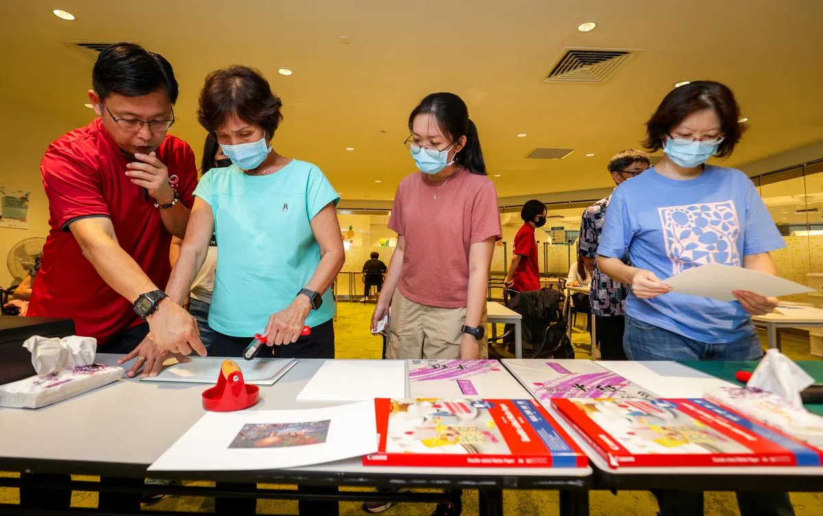 早报高级摄影记者梁麒麟（左一）也亲自指导读者进行图像转印工作，过程中需要将打印出来的蜡纸盖在宣纸上，再用卷轴在上面滚动碾压，就能把图像转印到媒介纸上。（叶振忠摄）