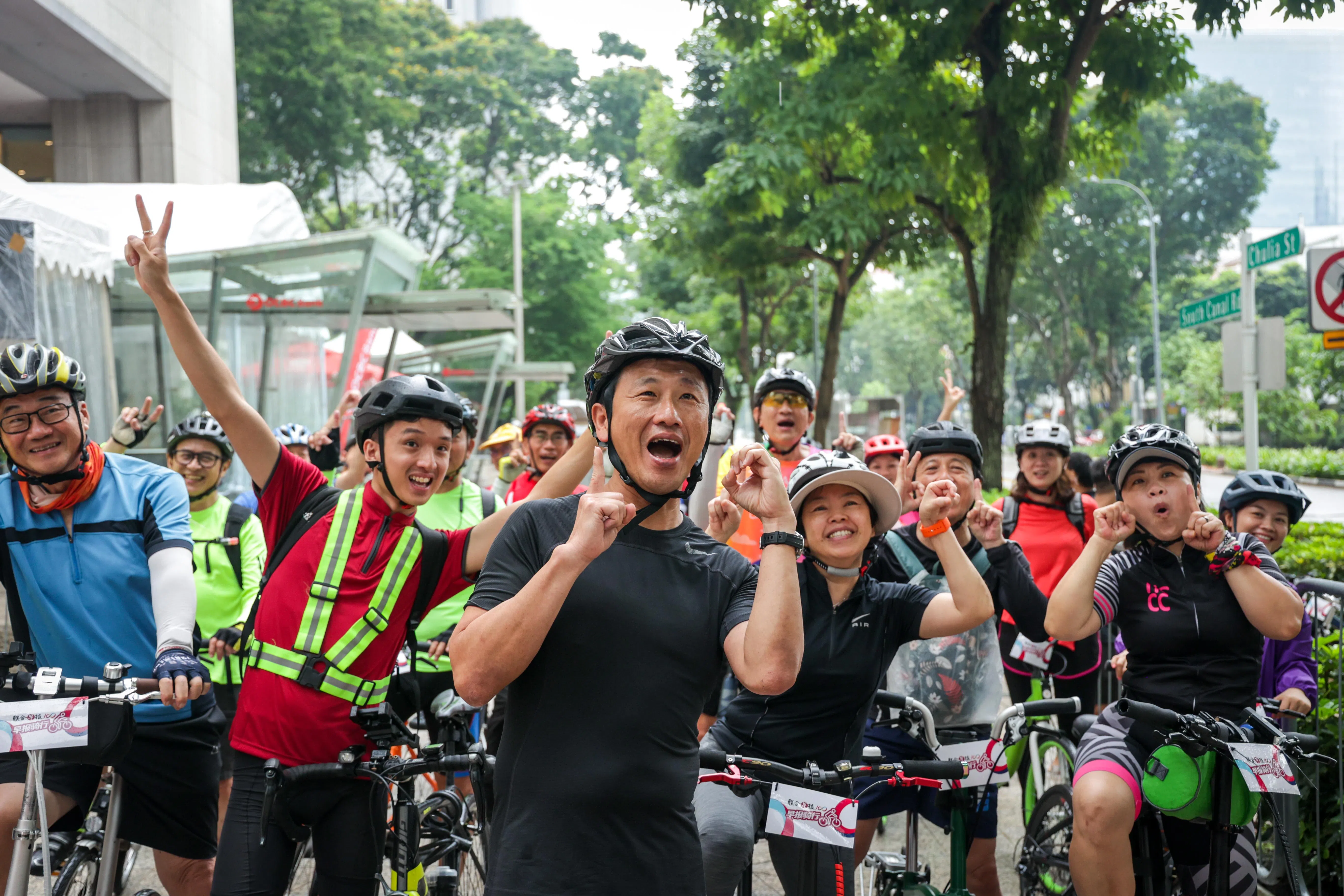 卫生部长王乙康（左三）带领着骑手们，手口并用摆出了“100”的字样，祝福《联合早报》百岁快乐。（叶振忠摄）