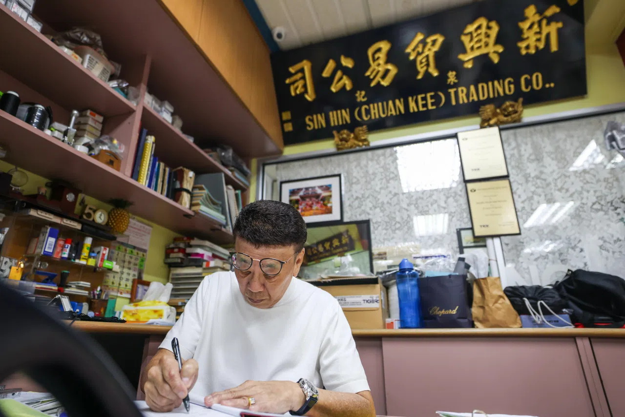 原店铺的招牌经过翻新后，挂在桥北路总店的办公桌后方，时刻提醒黄家子孙莫忘本。图为黄昭宝在店内处理订单。（白艳琳摄）