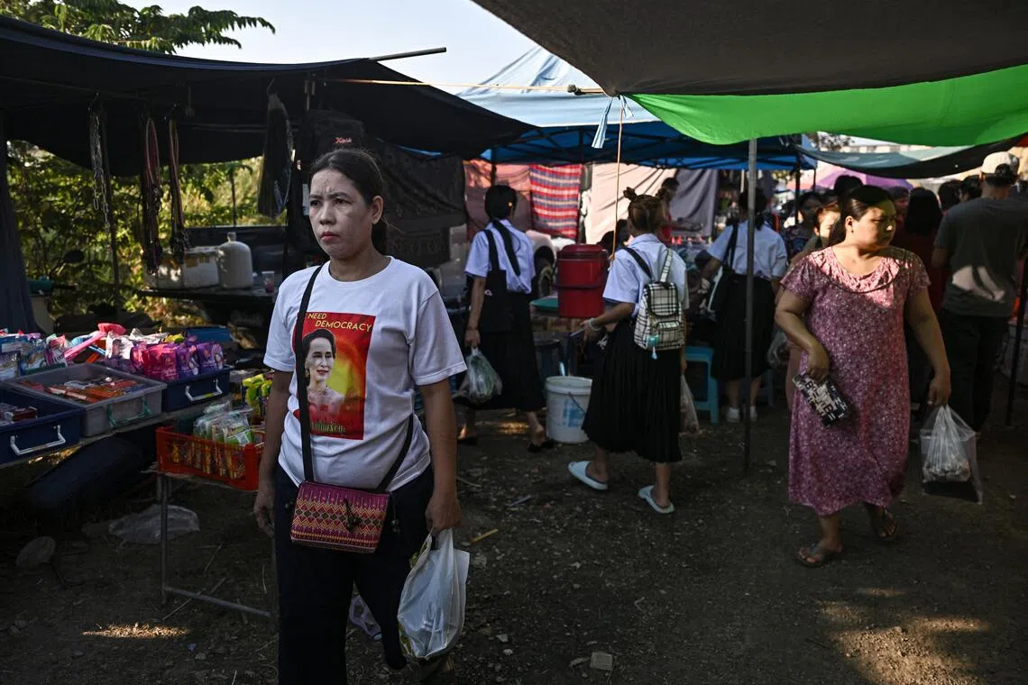 缅甸军方2021年发动军事政变后，国家深陷长达数年的血腥内战，数千名年轻人被迫逃往泰国寻求庇护。图为今年1月，一名身穿印有缅甸前国务资政翁山淑枝肖像衣服的女子，在泰国龙仔厝府（Samut Sakhon）的露天市场购物。这是缅甸移民工人经常光顾的市场。（法新社）
