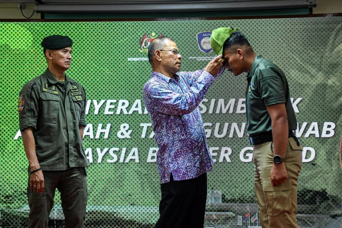 马国内政部长赛夫丁（中）星期一（4月13日）在马国边境卫队的成立仪式上，为加入卫队的退伍军人道菲（右）戴帽。左为马国边境管制与保护机构总监苏海里。（马新社）