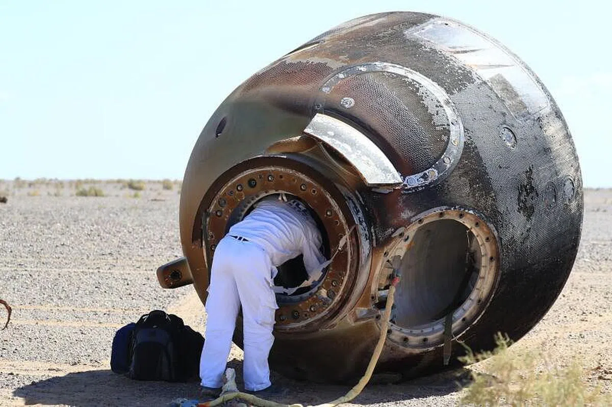 地面工作人员打开返回舱舱门，查看三名航天员的身体状况。（新华社）