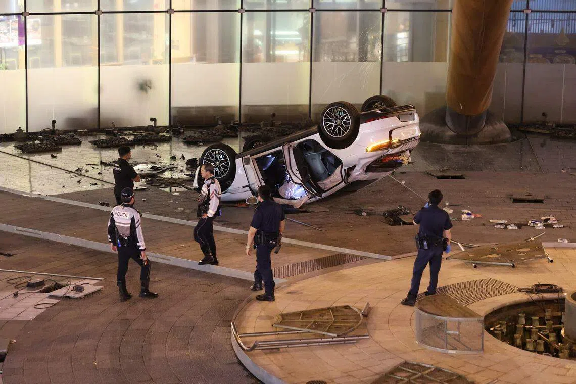 一辆汽车不知何故一头栽入新达城财富之泉后四轮朝天。（吴伟国摄）