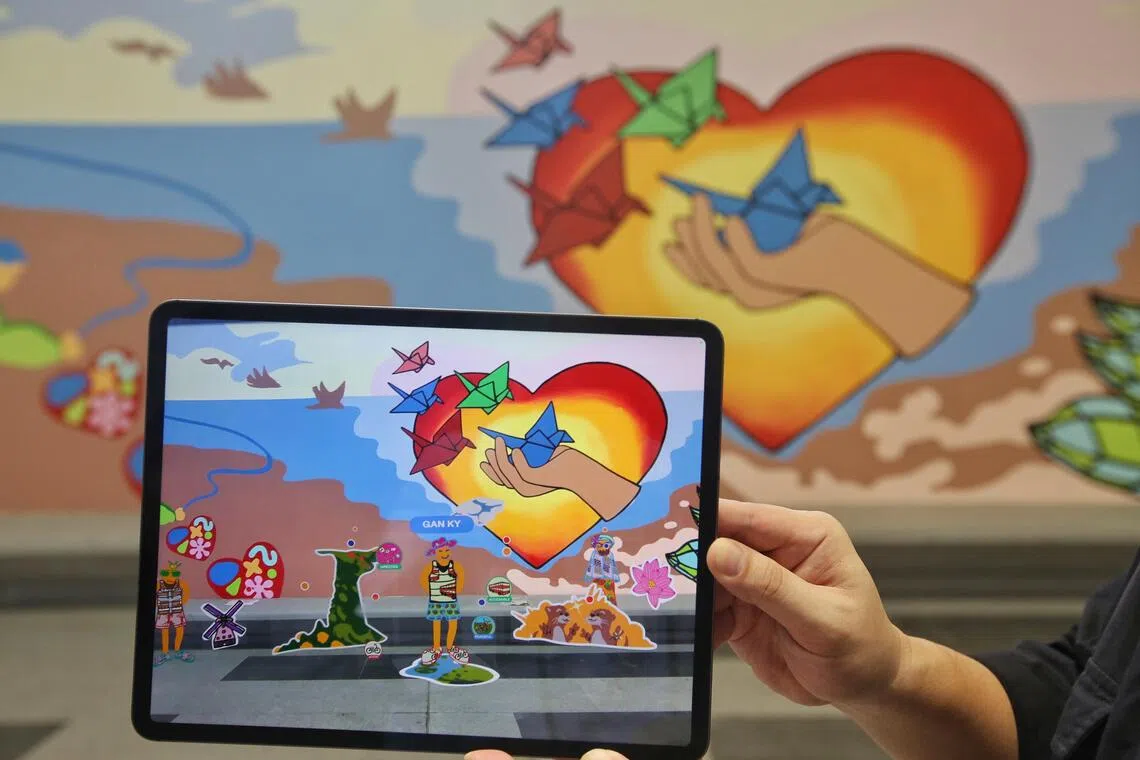 透过手机或平板电脑，公众可参与二次创作，观赏自己创造的虚拟角色或图像展现在壁画上。平板上正中穿着短裤的角色是副总理颜金勇创作的虚拟角色，而背景出现的心型图案则由特需艺术家陈睿恩创作。（特约陈福洲摄）