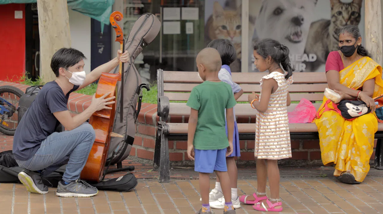 参与“音飨窗外”的大提琴演奏者陈文斌（左一）在淡滨尼社区表演独奏曲目，吸引不少路过的居民围观，他也趁录影空档，与一群好奇的小孩交流。（档案照片）
