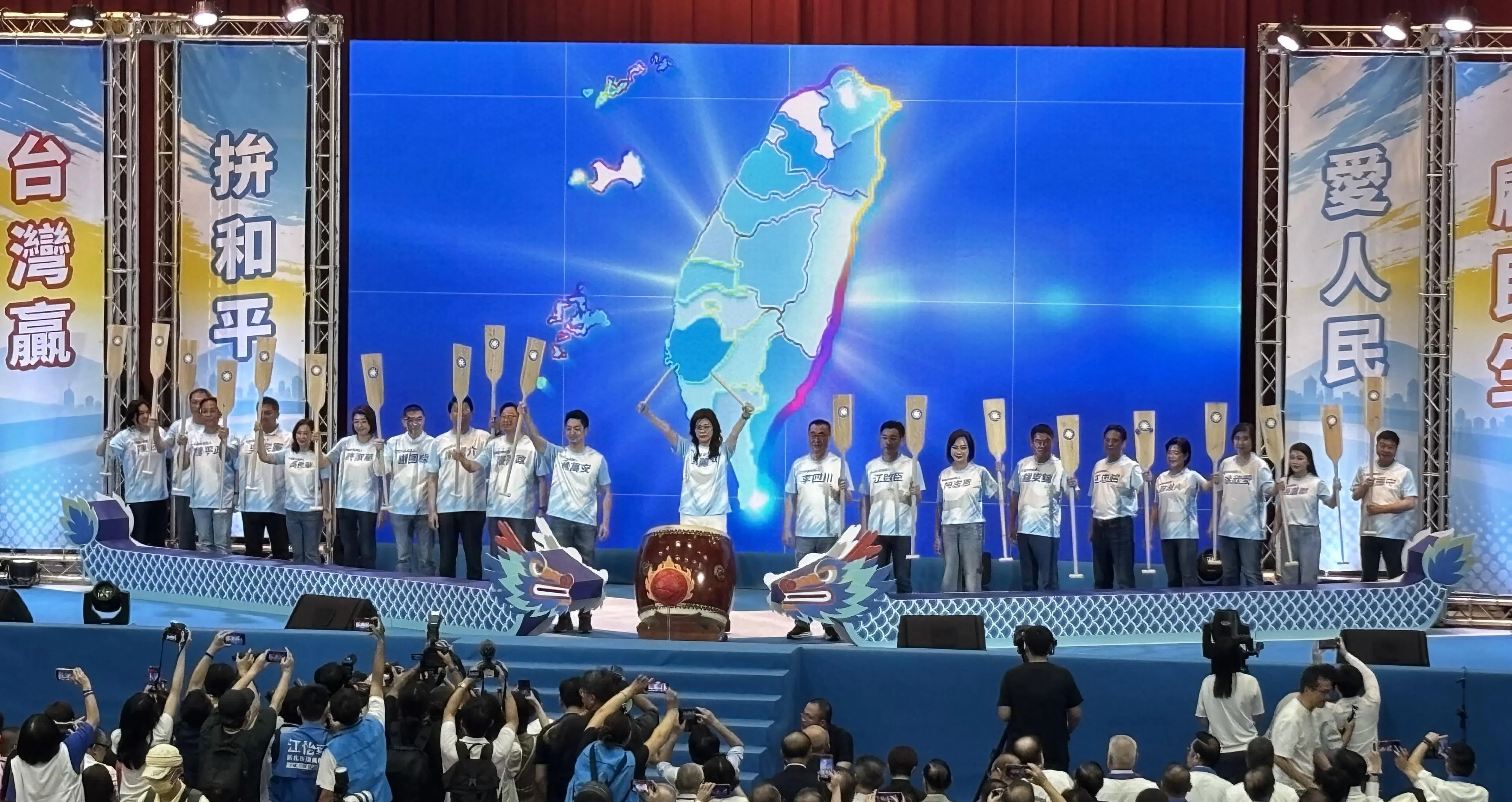 国民党主席郑丽文在全代会上击鼓，为2026年地方选举造势。19名县市长参选人手持船桨一字排开，象征全党同舟共济，迎战年底选举。（吕爱丽）