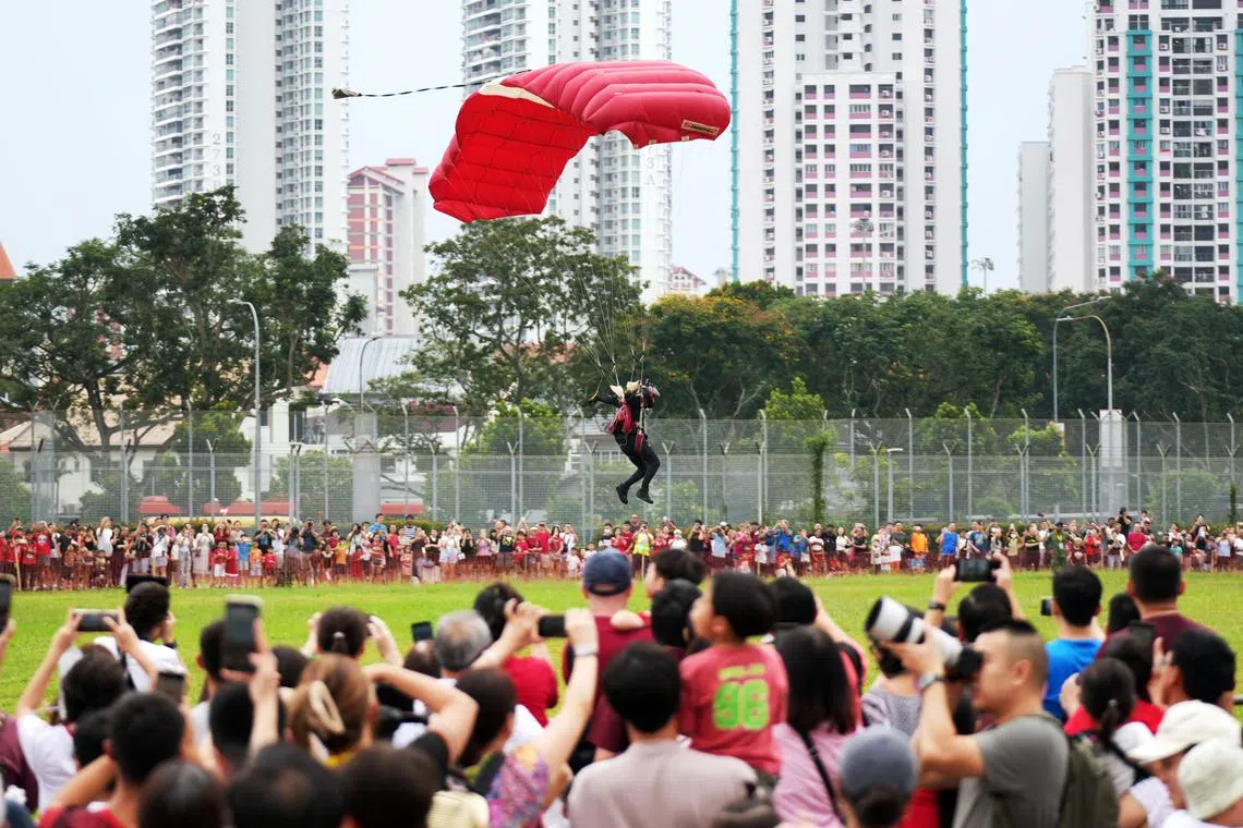 红狮跳伞队的队员带着红白降落伞在中区会场的草场上安全降落，现场观众以热烈掌声和喝彩迎接他们。（谢智扬摄）