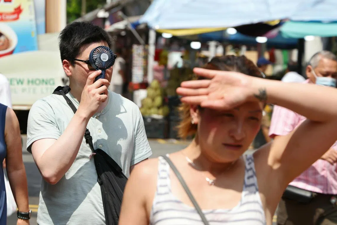 牛车水街道上呈现一副炎阳高照的景象，大批游客都打起了遮阳伞，有些行人还自带小风扇来降温。（梁麒麟摄）