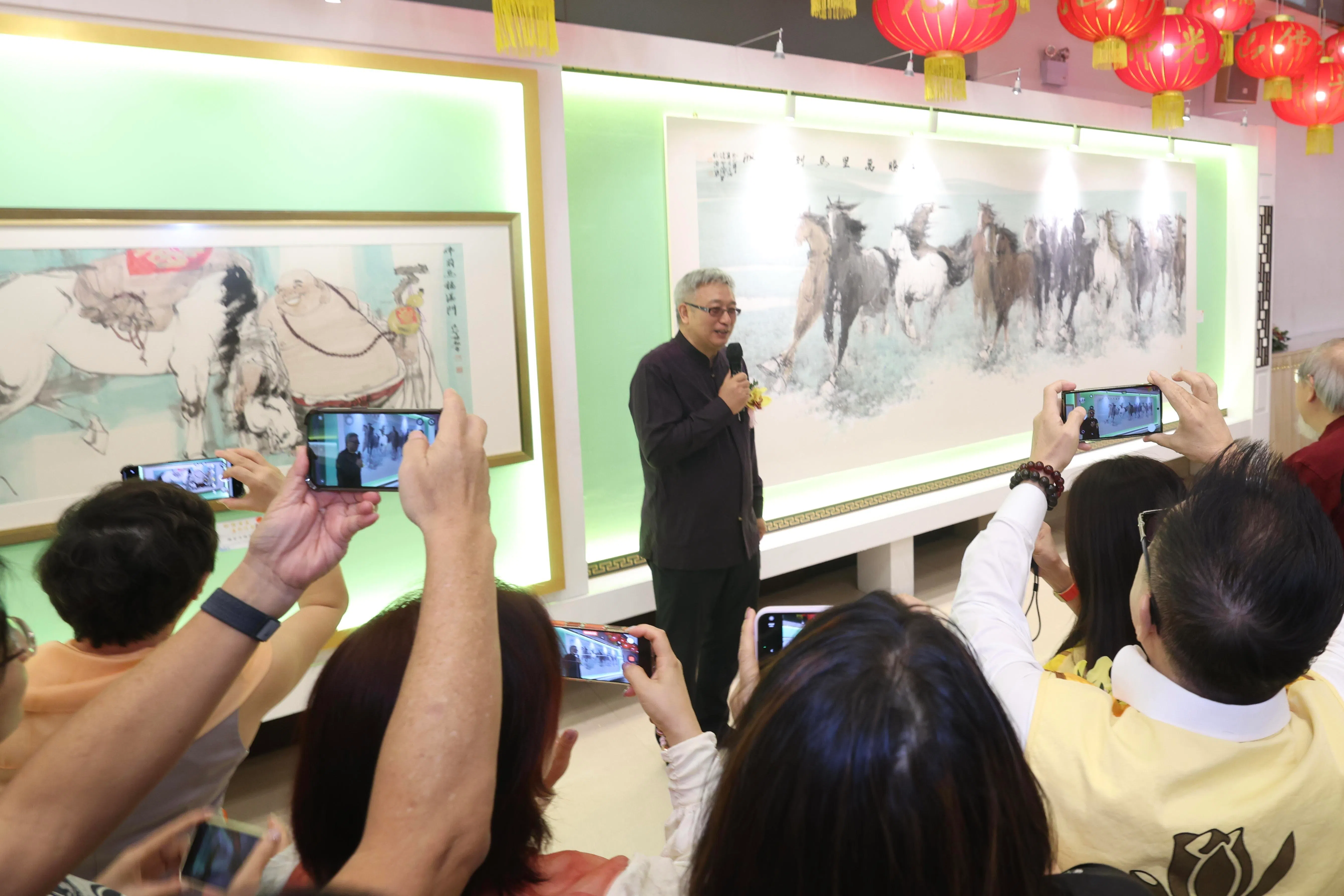 中国画家张智栋在新加坡佛光山，向参加画展开幕礼的宾客介绍他的《奔腾万里马到功成》画作（右边）。（郑一鸣摄）