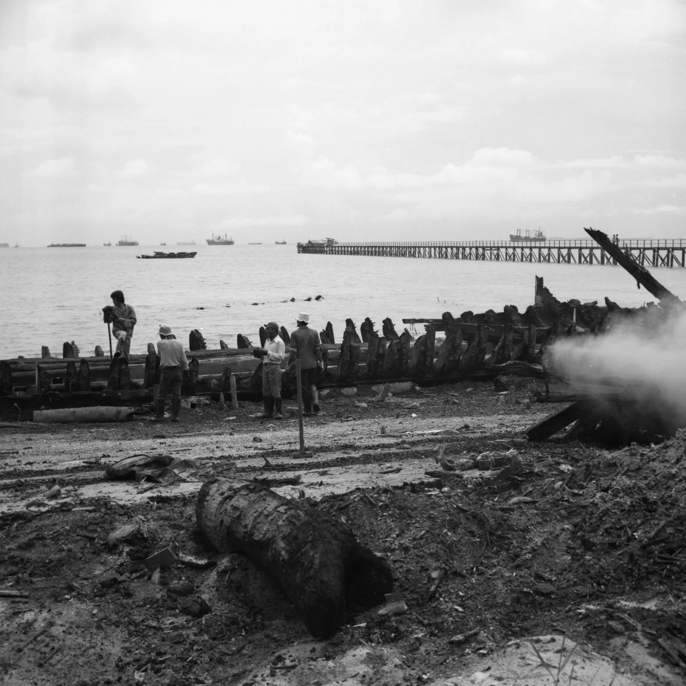 1982年，工人在实马高岛海边检查一艘木船以便焚化，前景为木船焚化后的遗骸。（Geoffrey Benjamin提供）