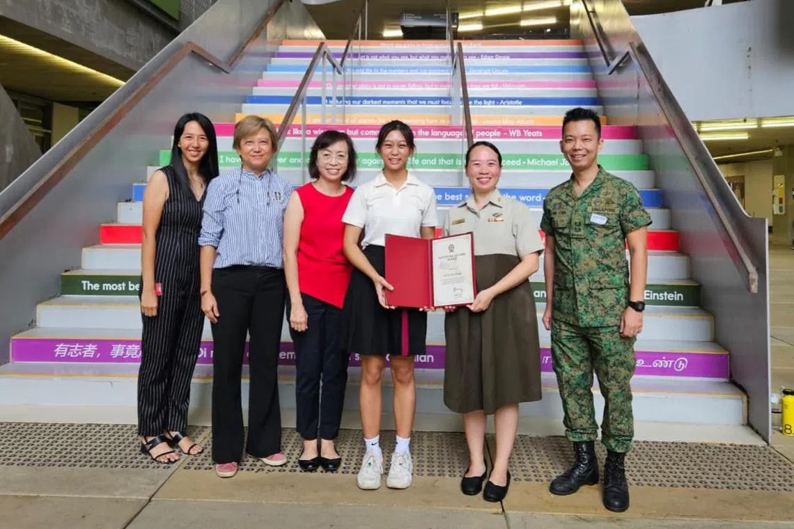 陈依宁（图中身穿白衣半裙女生）在2024年荣获新加坡武装部队青年领袖奖。站在她右侧的是新加坡艺术学院师长，左侧是国防部军官。（受访者提供）