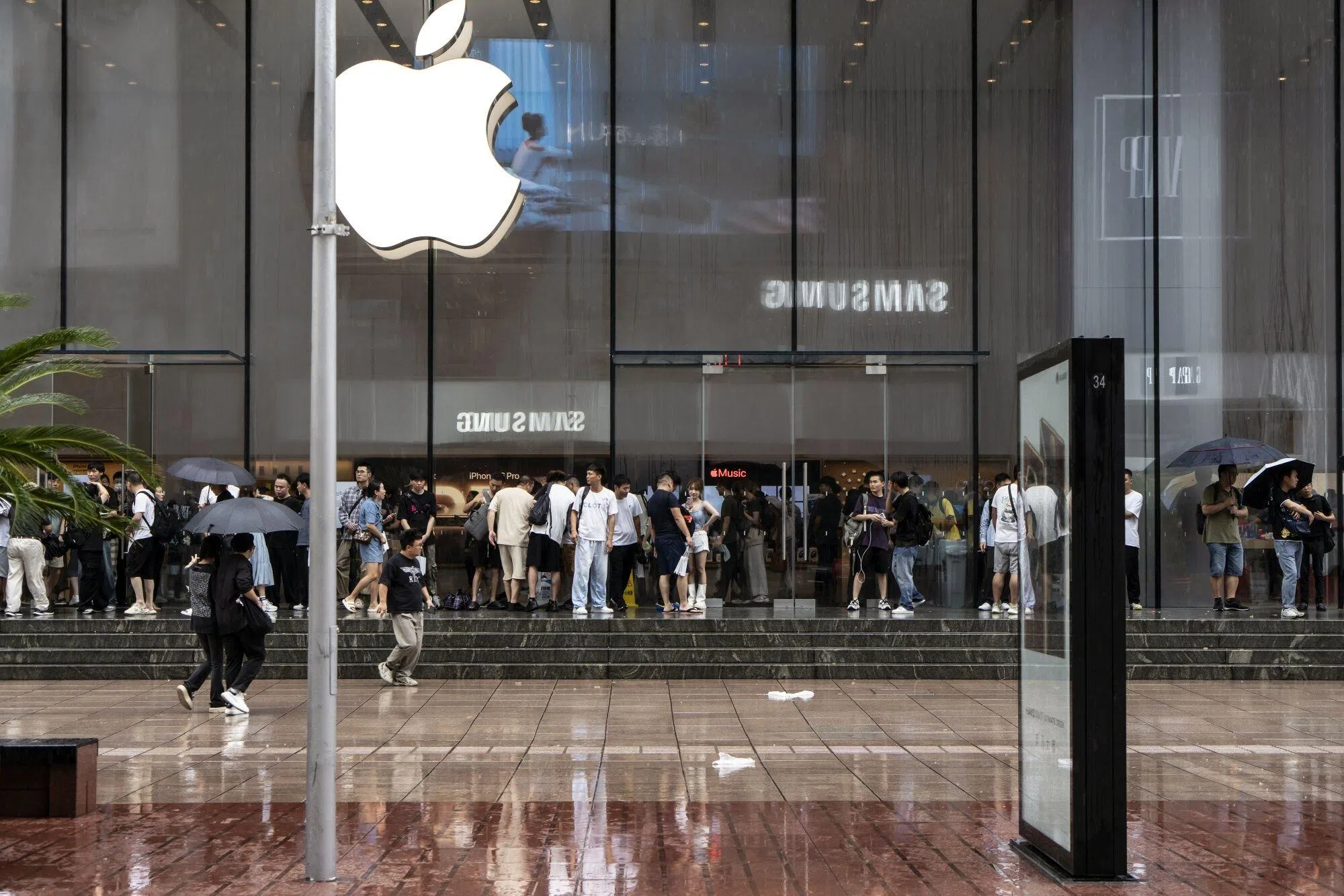 苹果最新推出的iPhone 16系列旗舰机星期五在中国上市，图为上海民众在苹果旗舰店外冒着雨排队。（彭博社）