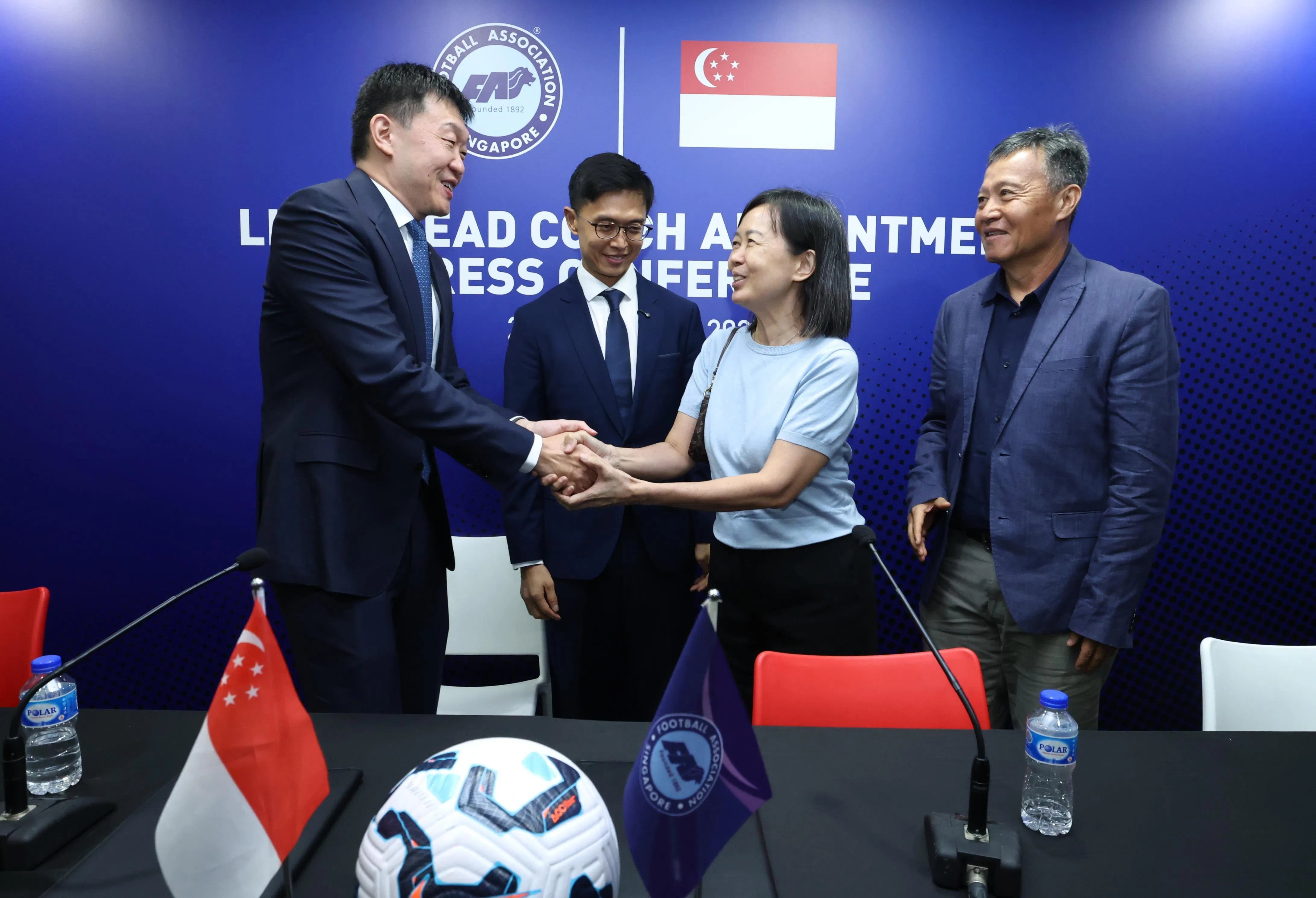 李斯平（左二）上任雄狮主教练后，足总会长李小冬（左一）向到场的李斯平母亲钟丽琼（右二）和父亲李国兴表达祝贺。李国兴也是足球教练，自2012年在维多利亚初级学院女子队任教。维初女队在今年达成全国校际运动会女足A级11连冠。（梁麒麟摄）