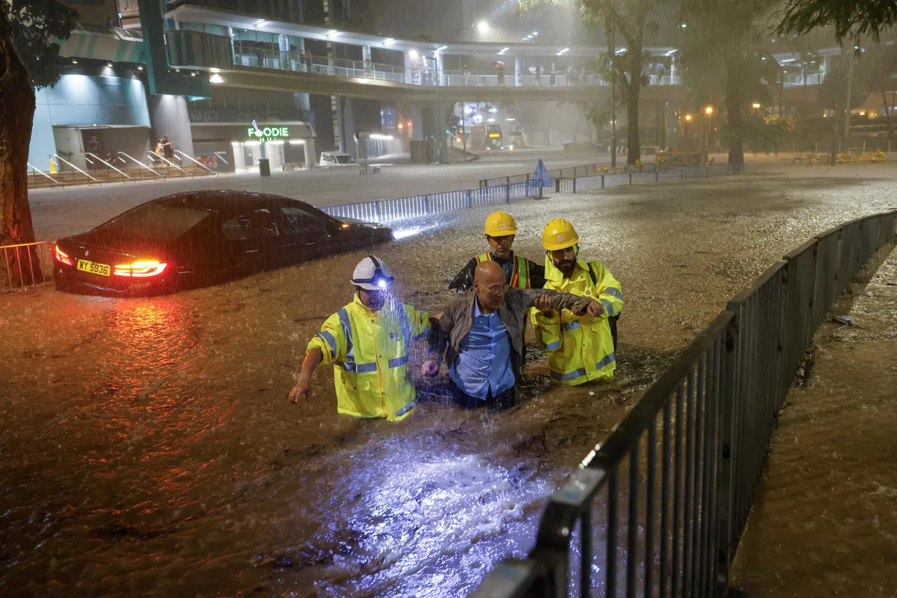 香港消防和警方在暴雨期间接获逾千宗求助，图为救援人员在暴雨中协助一名被困的司机。（路透社）
