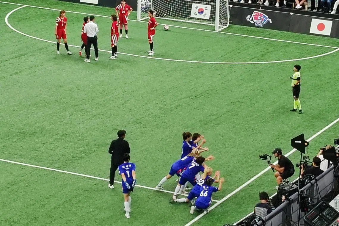 日本球员（蓝衣）进球后，对着摄影机庆祝。韩国球员（红衣）则检讨丢球及为后续比赛做准备。（陈明耀摄）