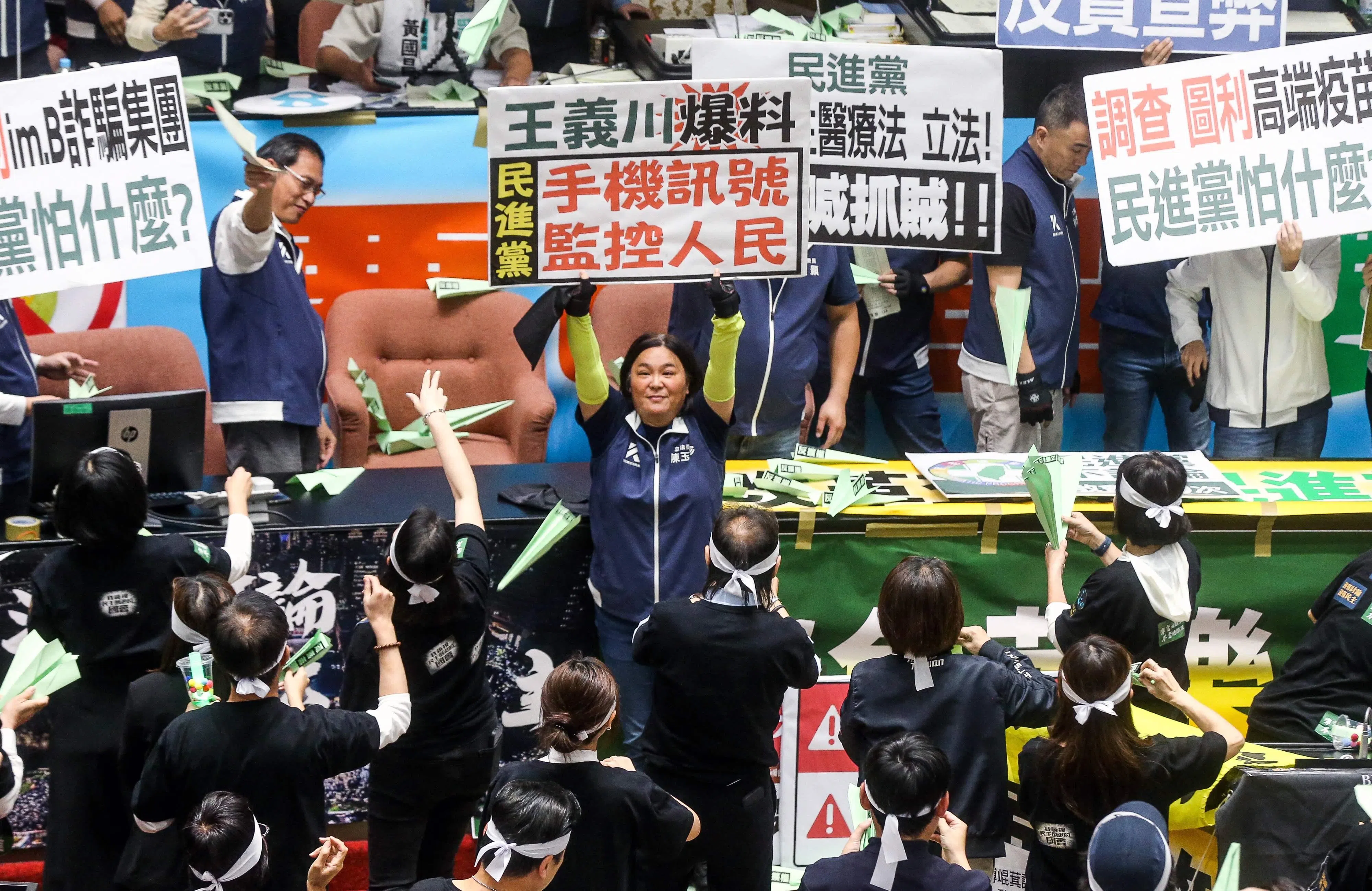 国民党立委陈玉珍（中）星期二在立法院内高举抗议字牌，批评民进党利用手机讯号监控人民。另一端民进党立委则向主席台上射出绿色纸飞机。（法新社）