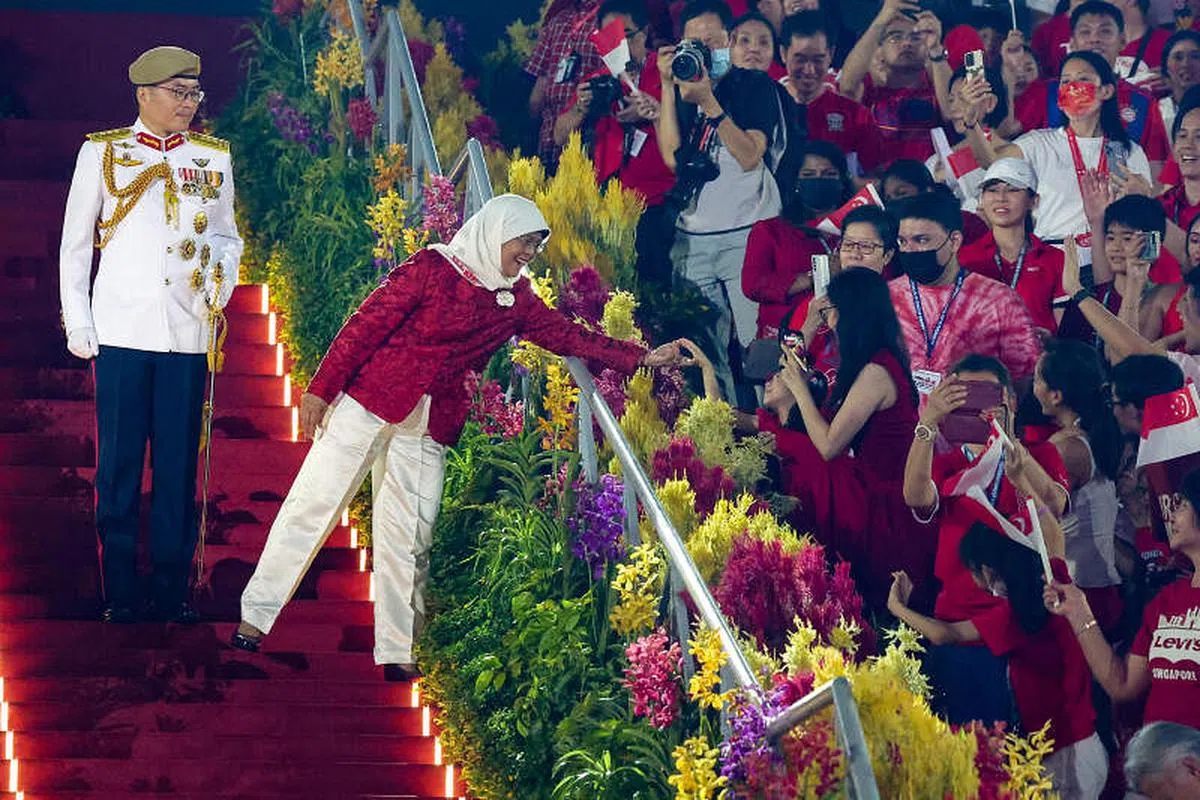 离开庆典现场前，哈莉玛总统（左二）在三军总长王赐吉中将（左一）的陪同下步下台阶，途中与观众席里的小朋友亲切搭手问好。（白艳琳摄）