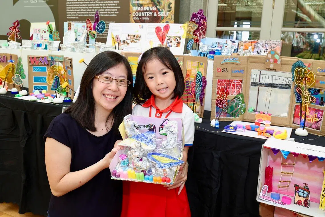 刘利思和女儿李芊卉的背后，是女儿和30多名同学用多种材料制成的一个共享社区模型，母女手里拿着的是李芊卉参与制作的其中一部分：创意小贩中心座椅。（周国威摄）