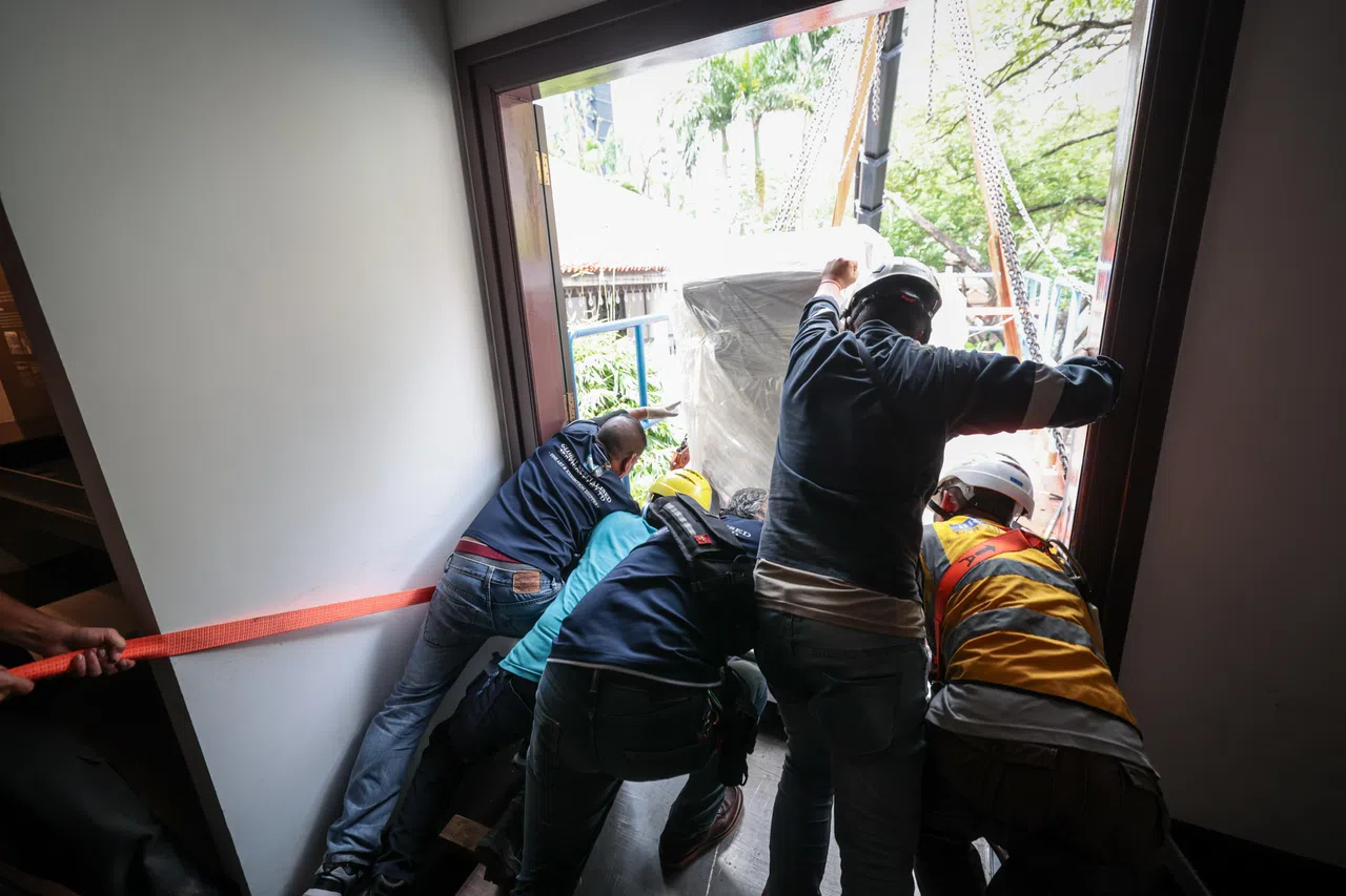 印刷机底部固定好在专属定制的铝板支撑台后，再由五个员工协力推向楼外的平台，同时还要确保不会碰到机器较为脆弱的零件部位。（张俊杰摄）