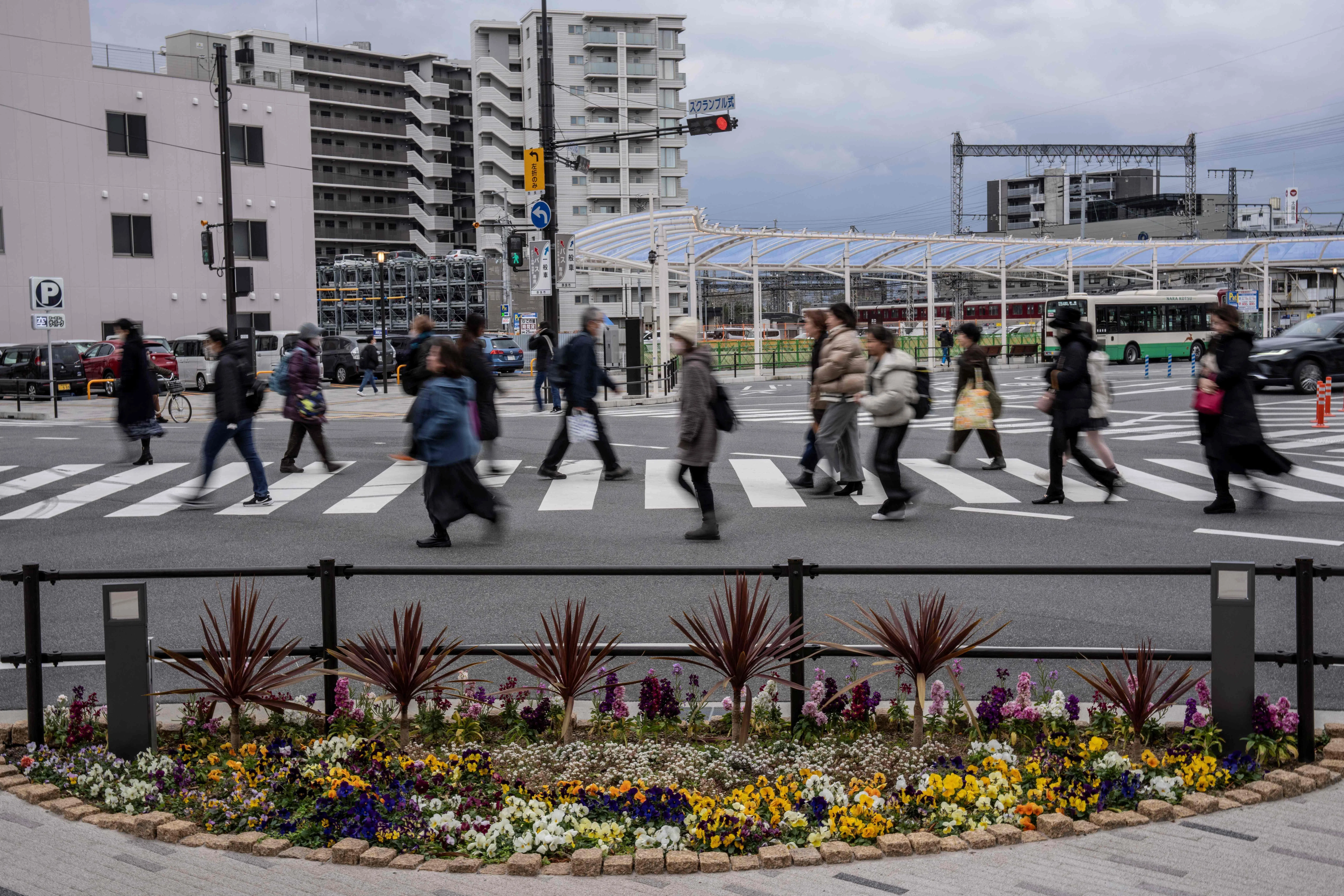 1月13日，人们走过位于奈良市近铁大和西大寺站前十字路口的一处花坛纪念地。此处是日本前首相安倍晋三在发表竞选演讲时遭枪击身亡的地点。（法新社）