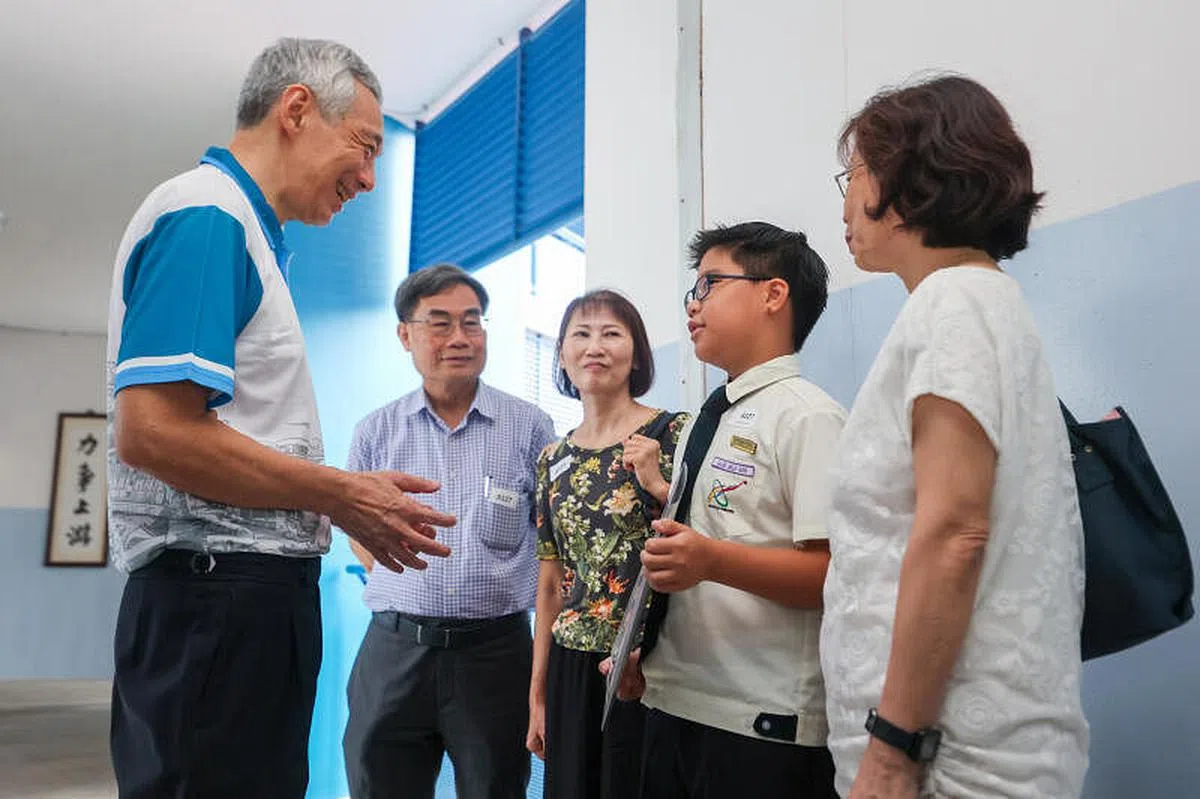 李显龙总理（左一）星期六早上在第一场宏茂桥德义区教育助学金颁奖礼后，与获奖学生与家人互动，其中包括获颁教育储蓄品德奖的小五学生吴捷乐（右二）。（陈斌勤摄）
