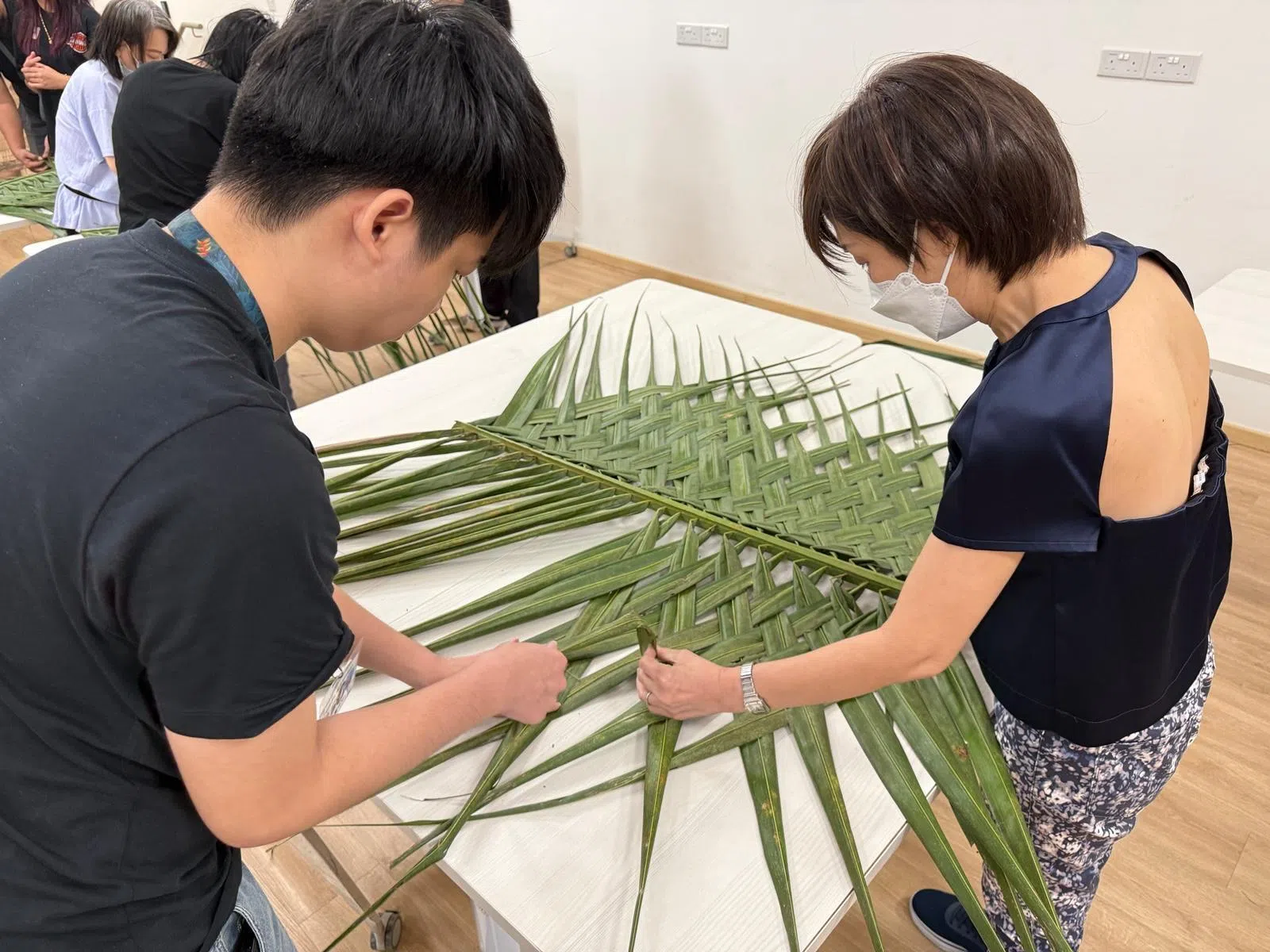 王玉珠（右）陪儿子参加由飞跃社服机构为心理疾病患者主办的户外活动，学习如何照顾鸟禽，其中一堂是学习用椰叶编织成鹦鹉的益智玩具。（受访者提供）