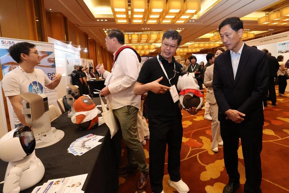 社会政策统筹部长兼保健卫生部长王乙康（右一）参观新加坡慈怀疗护大会的展位，向工作人员了解人工智能社交机器人LOVOT如何操作。（梁麒麟摄）