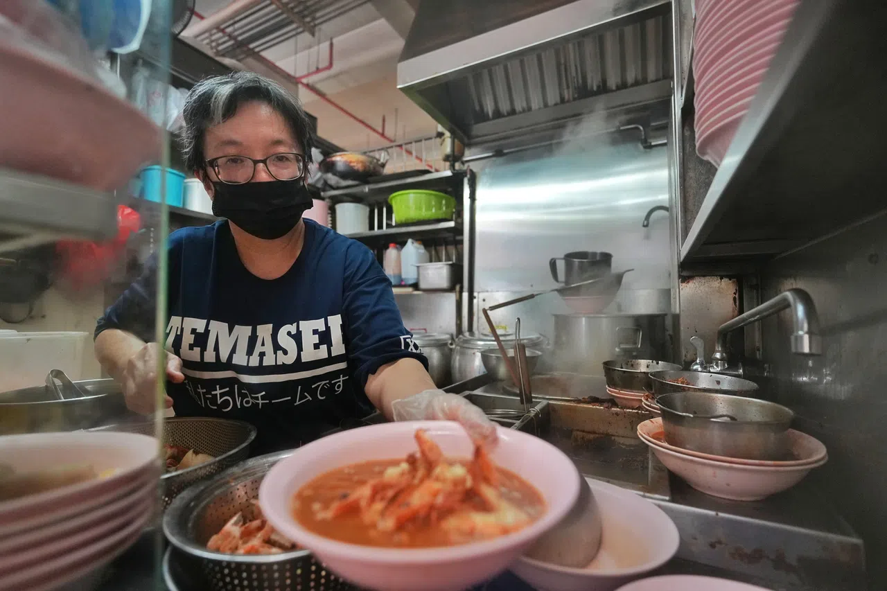 威利大虾面第二代摊主之一的何锋泉与妻子林翠英（图）多年来仍坚守在旧机场熟食中心，为食客烹煮虾面。（谢智扬摄）