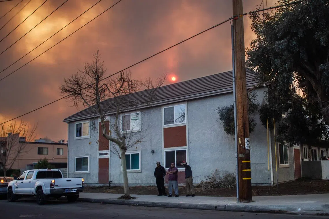 洛杉矶县向3万多居民发出疏散令。1月22日，卡斯泰克社区的居民站在自家门外，天空中弥漫着休斯大火造成的浓烟。（法新社）