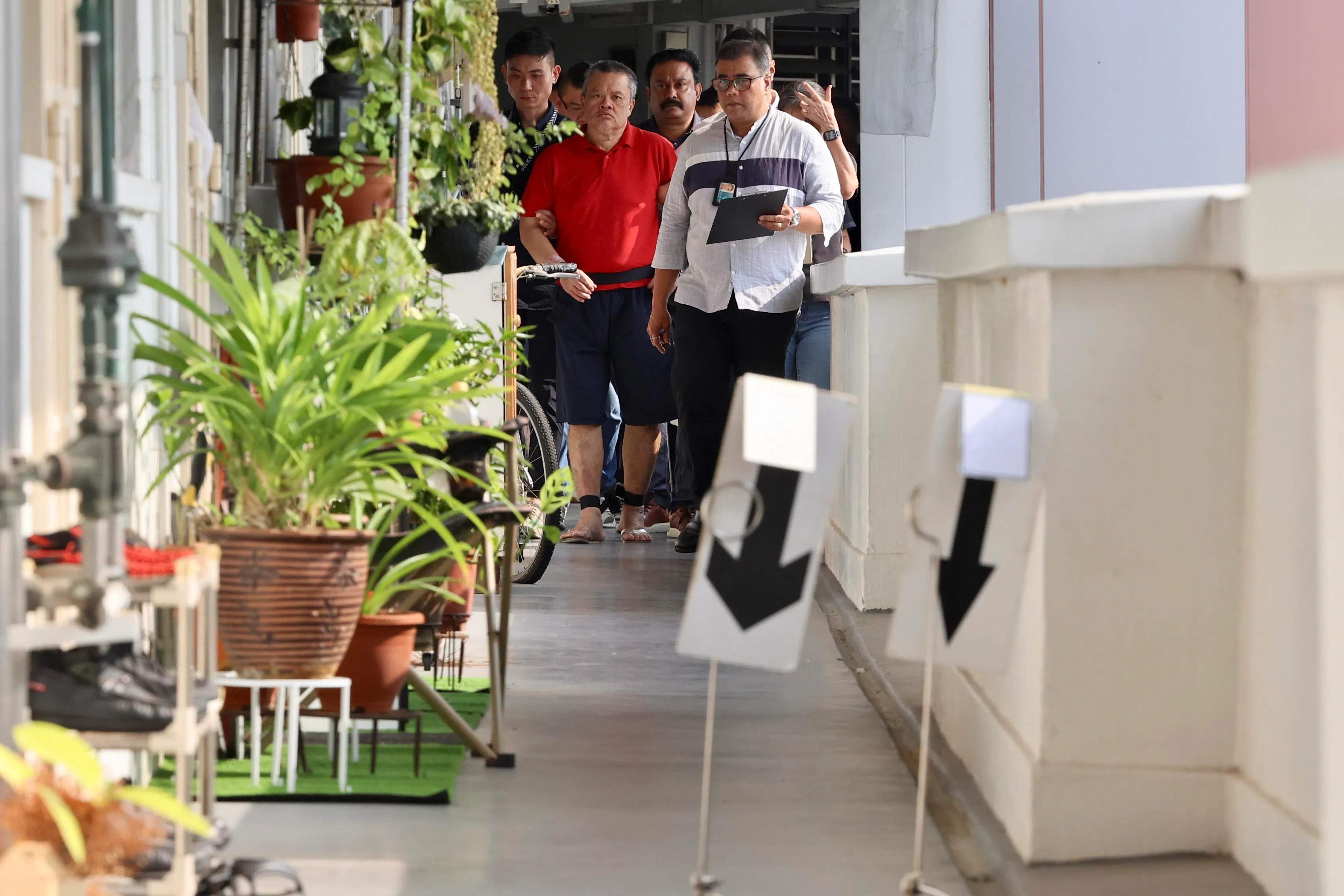 被告身穿红色上衣和蓝色短裤的黄瑞成，在约六名警员押送下抵达现场。（邝启聪摄）