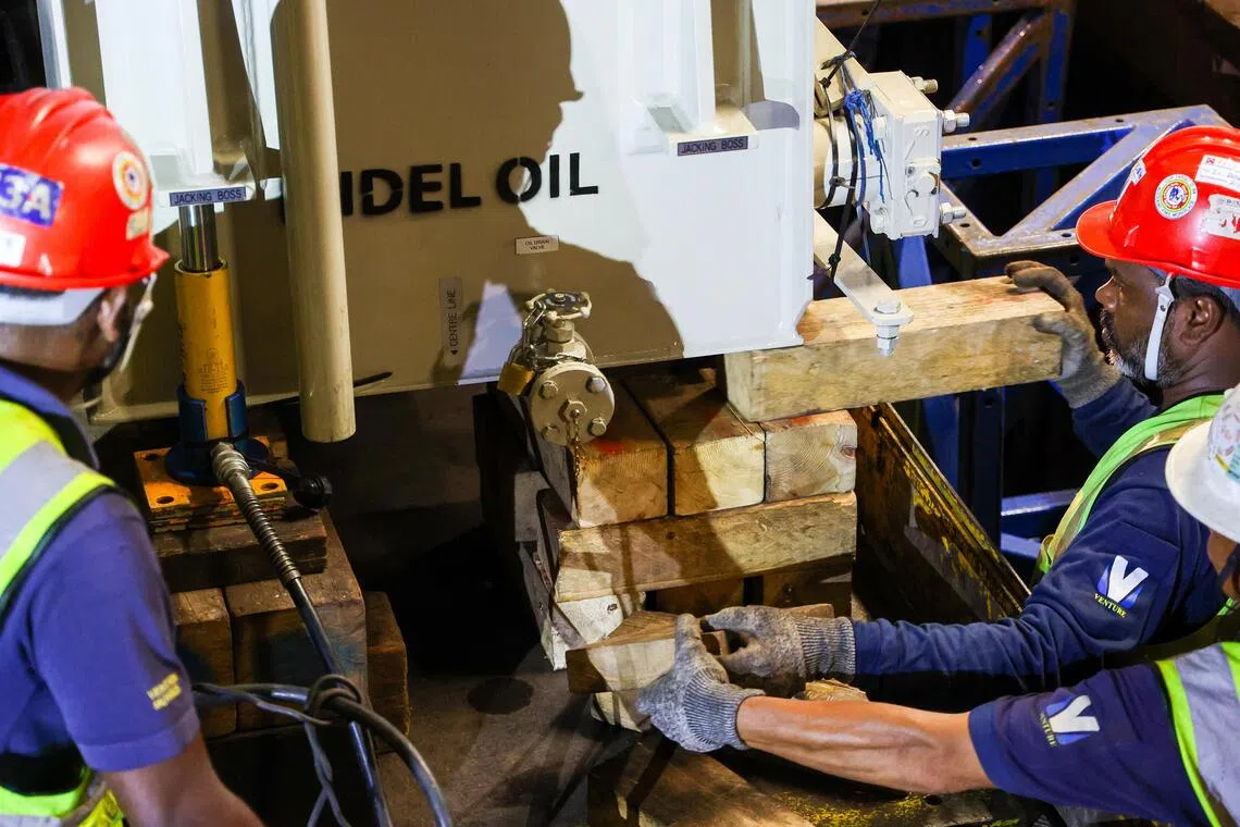 多名施工人员配合，使用千斤顶抬起整流变压器，再用木块把它垫高至与站台齐平，才能将它拉入变电室内。（林明顺摄）