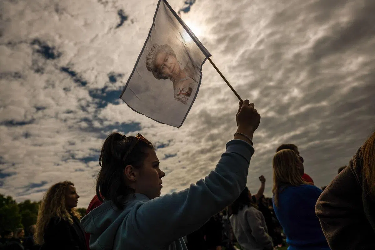 一名女子在伦敦海德公园观看伊丽莎白二世国葬直播，挥舞着一面印有女王肖像的旗帜。（路透社）