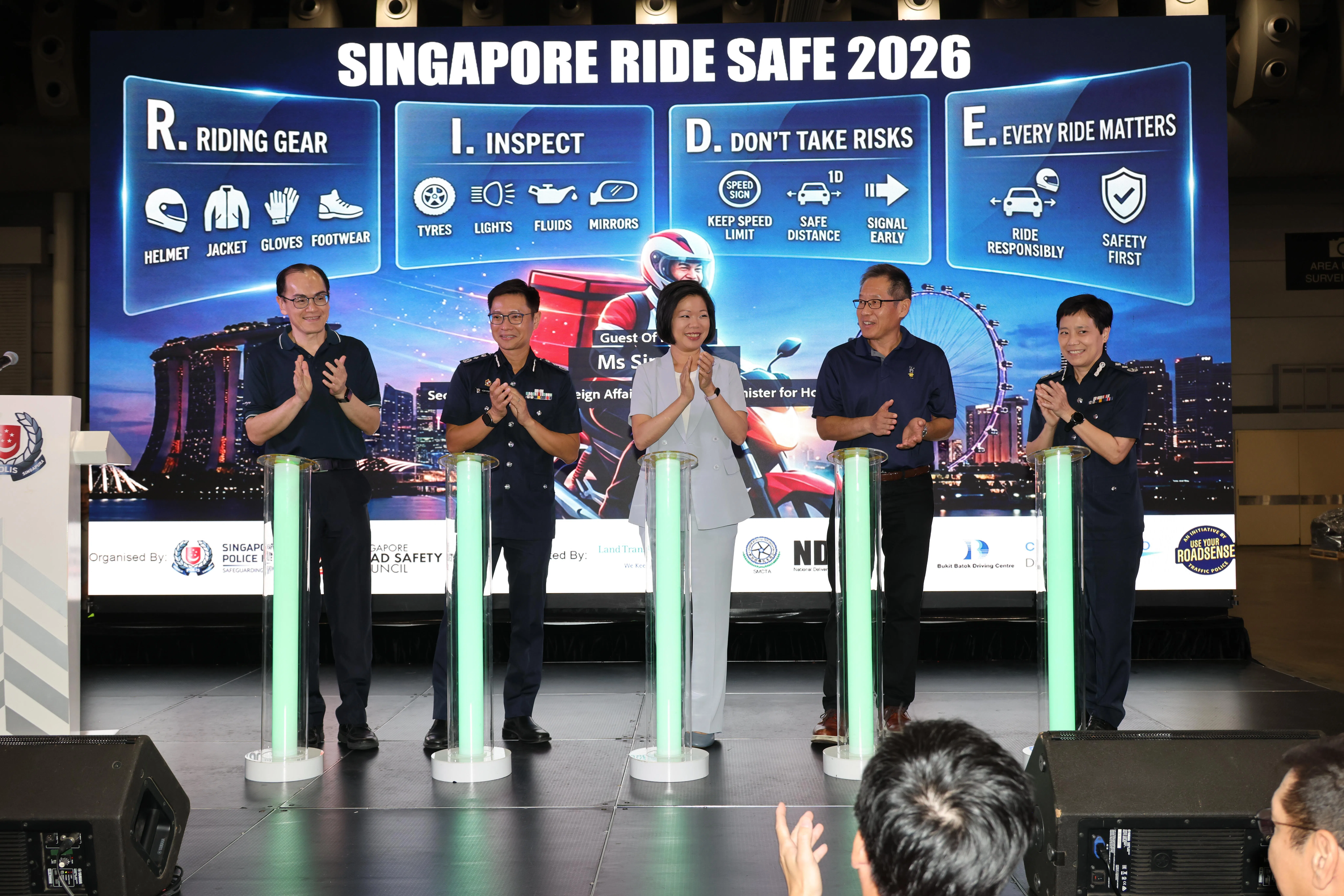 交警推出的全新“R.I.D.E.”宣传海报，将在送餐平台应用、商场的电单车停车场及其他公共场所展示。陆交局候任副总裁（企业与发展）谢明德（左起）、警察总监侯光辉、外交部兼内政部第二部长沈颖、新加坡公路安全理事会主席⁠高泉泰和交通警局局长周利玲高级助理警察总监星期六（9月12日）在活动上揭示新的海报。（梁麒麟摄）
