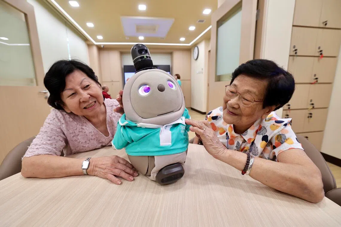 80岁的朱宝珠（左）星期五（1月30日）首次接触陪伴型机器人LOVOT后，认为它非常逗趣和乖巧，能够给她解闷，但她还是比较喜欢人与人之间的交流。图为朱宝珠与另一年长者谈锦芳（88岁）在牛车水的Sparkle Care乐龄护理中心同LOVOT互动。（陈斌勤摄）