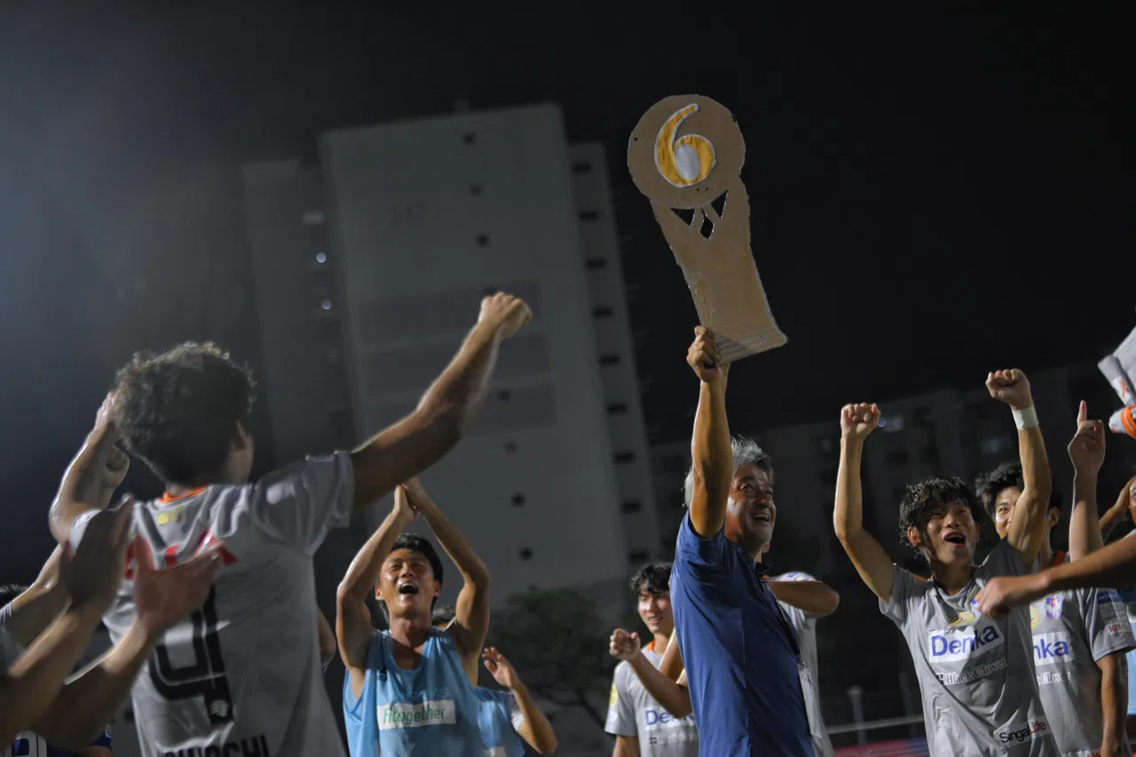 新潟队主帅吉永一明（蓝衣）在赛后举起纸板奖杯，和球员庆祝球队夺冠。（海峡时报）