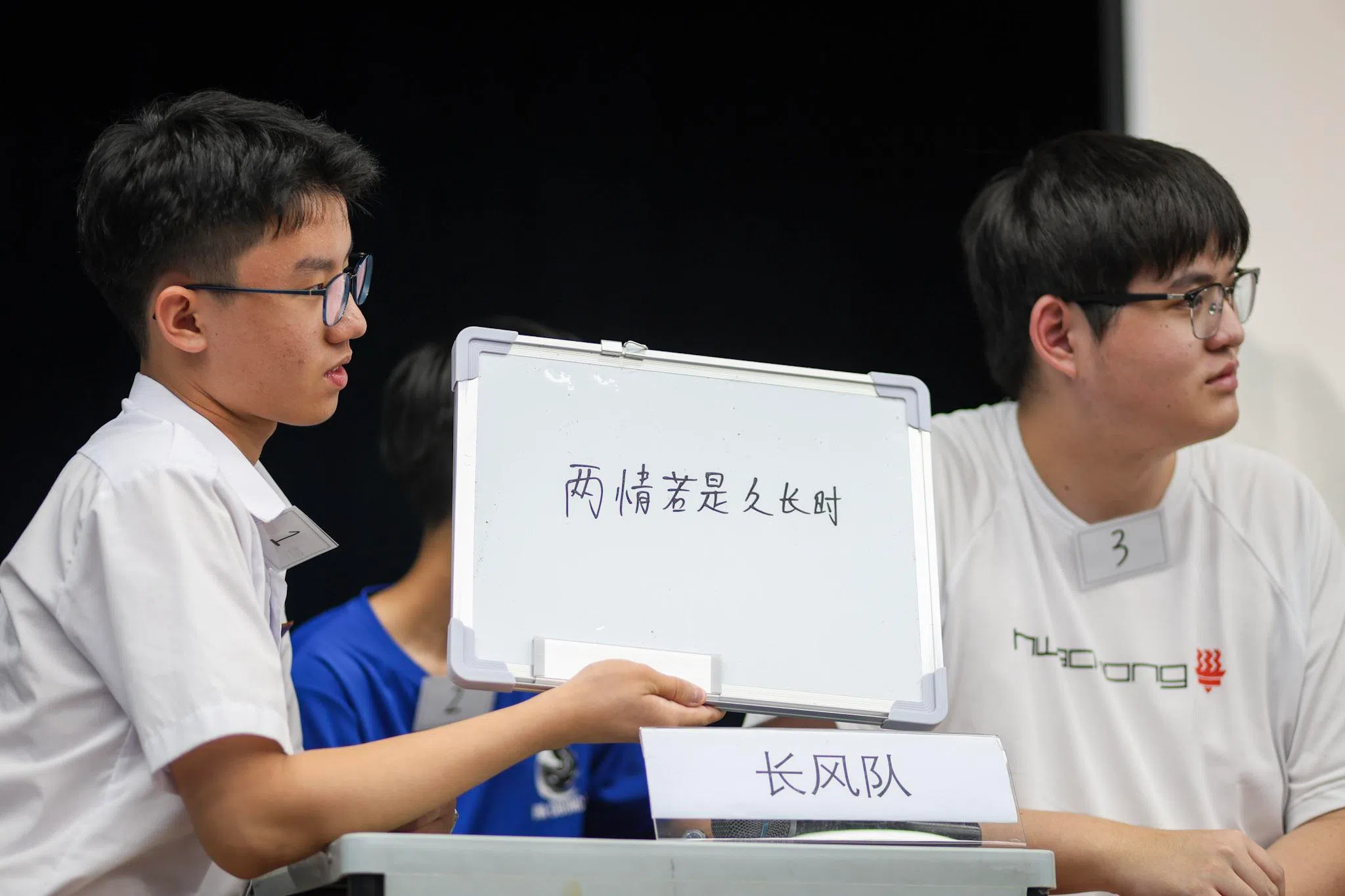 在“穿针引线”环节中，“长风队”的吴曜轩（左一）亮出写在白板上的答案，让主持人检查。（华侨中学高中部袁闻伯摄）