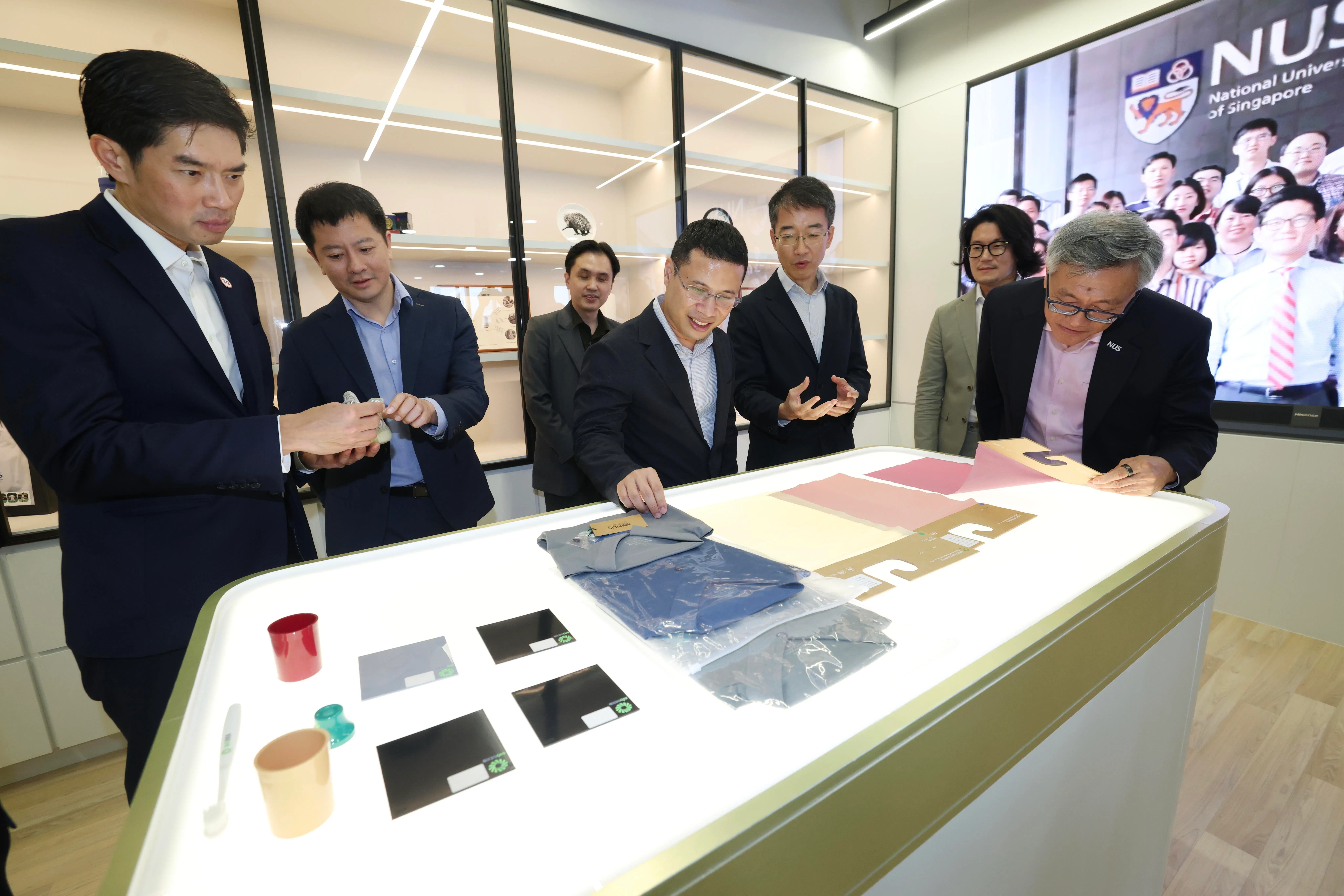 教育部长李智陞（中）与新加坡经济发展局局长黎佳明（左起）、国立研究基金会副行政总裁陈伟哲、国家工程生物学中心副理事长傅觉鲁副教授、国家工程生物学中心助理研究员薛博研究助理教授、国家工程生物学中心执行理事长兼国大合成生物学创新研究项目主任张旭教授和国大校长陈永财教授，一同参观国家工程生物学中心的设施。桌上展示的物品由生物基材料制成。（郑一鸣摄）