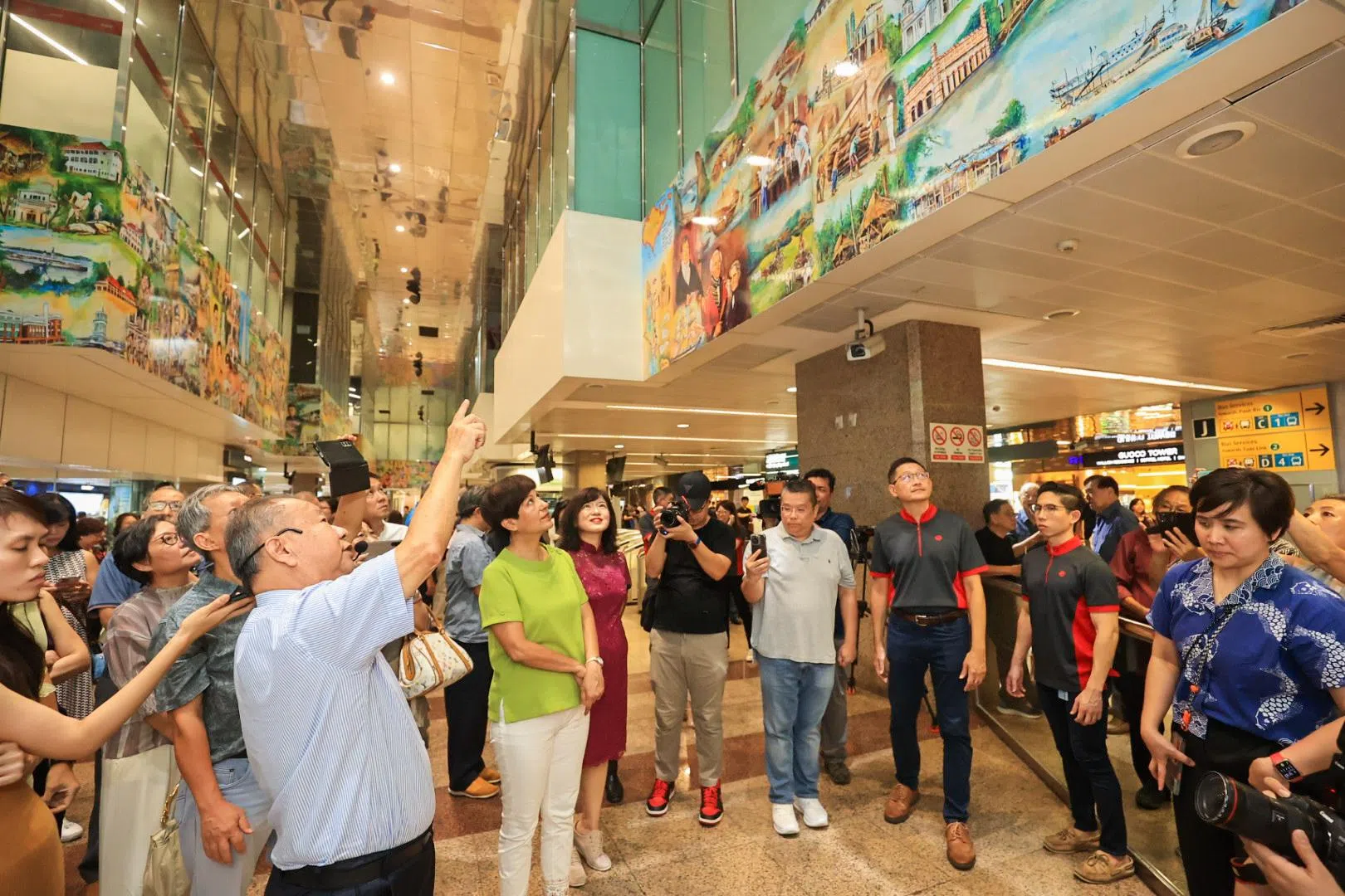 艺术家黄品胜（左）向活动主宾总理公署部长兼财政部及国家发展部第二部长英兰妮（身穿绿衣）讲解壁画的创作概念。（吴先邦摄）