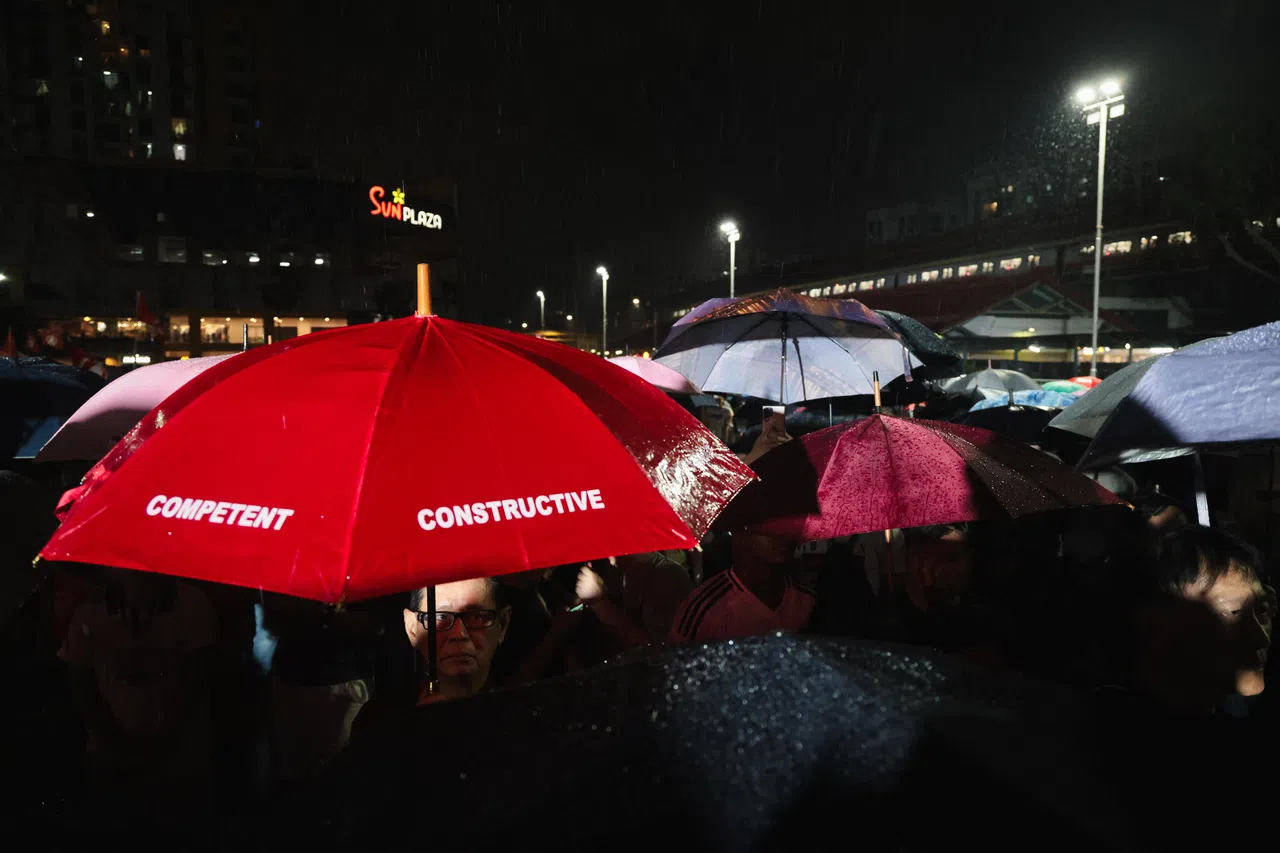 本届大选恰逢季候风潮，群众大会举行期间全岛多处猛下强降雨。民主党4月27日晚间在三巴旺地铁站和太阳广场（Sun Plaza）旁的硬地球场举行群众大会，不少民众在暴雨中撑伞听演说，五颜六色的雨伞为情绪激昂的政治场地平添柔和色彩。（张俊杰摄）