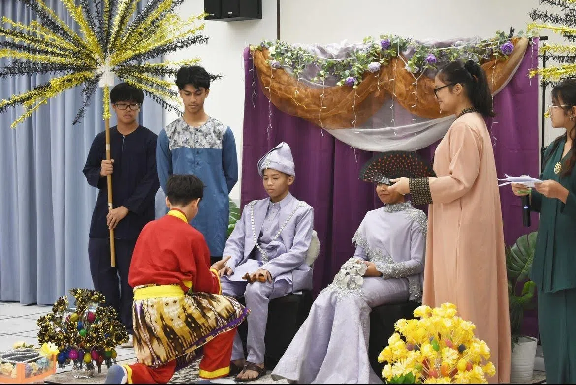 马来学生进行模拟婚礼 “一日皇帝” 仪式，两名身穿紫色衣服的学生扮演婚礼中的新郎新娘。（长老会中学提供）
