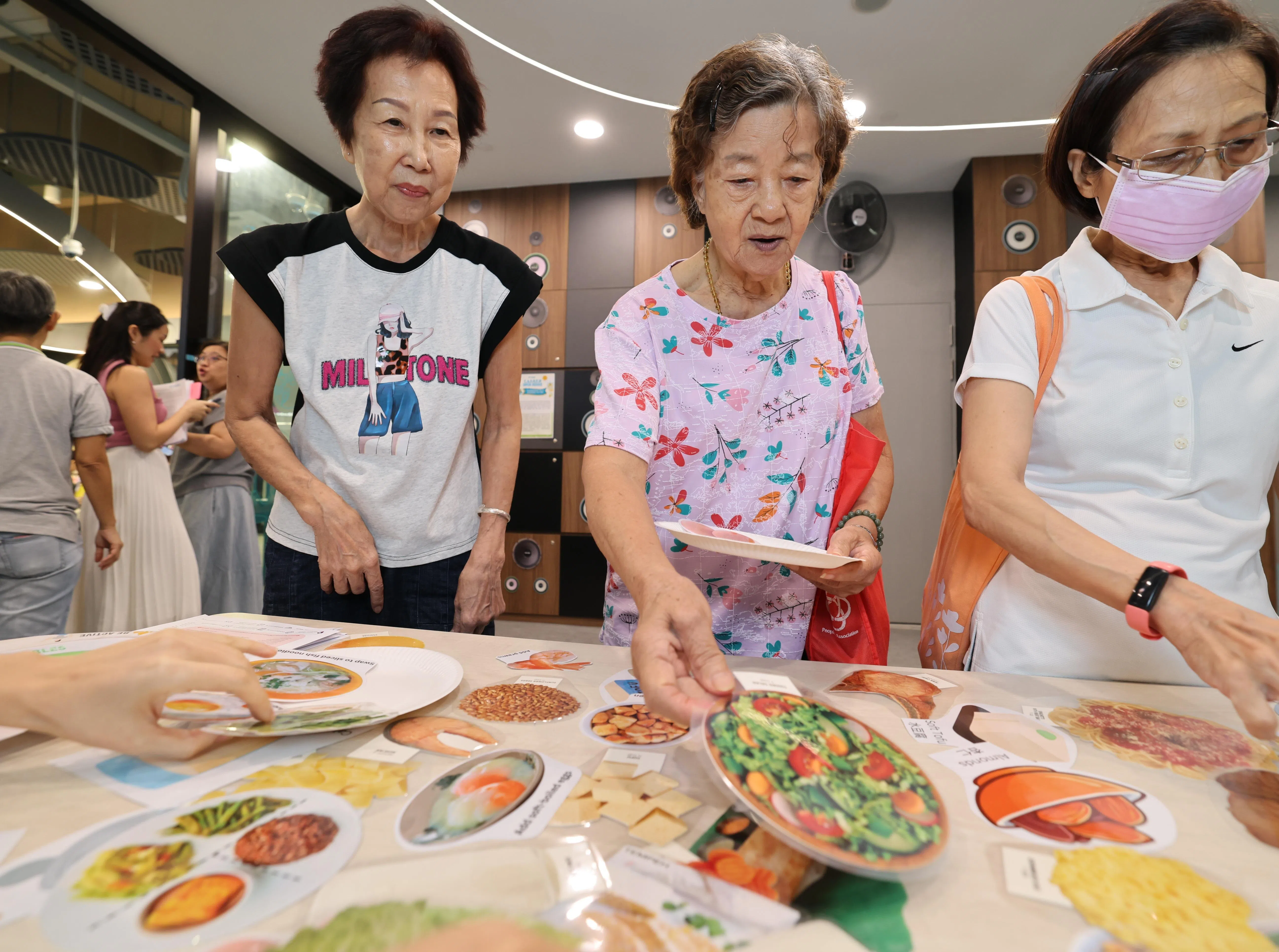 武吉班让居民洪裕妹（75岁，左起）和卓来金（88岁）结伴出席职总保健活跃乐龄中心开幕仪式。两人通过老年教育与研究院摊位的互动游戏，了解均衡饮食的重要。（梁麒麟摄）